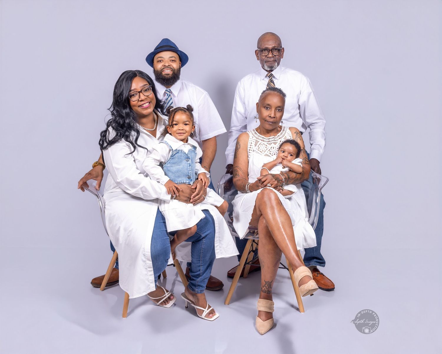 Family portrait of six people in white and denim outfits, including two babies, posed in a studio setting.