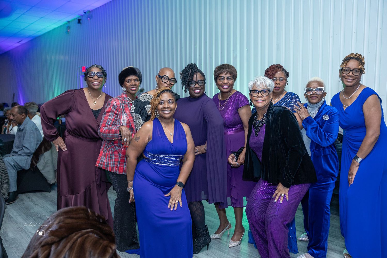 A group of women posing together in purple and blue outfits at a formal evening gala event.