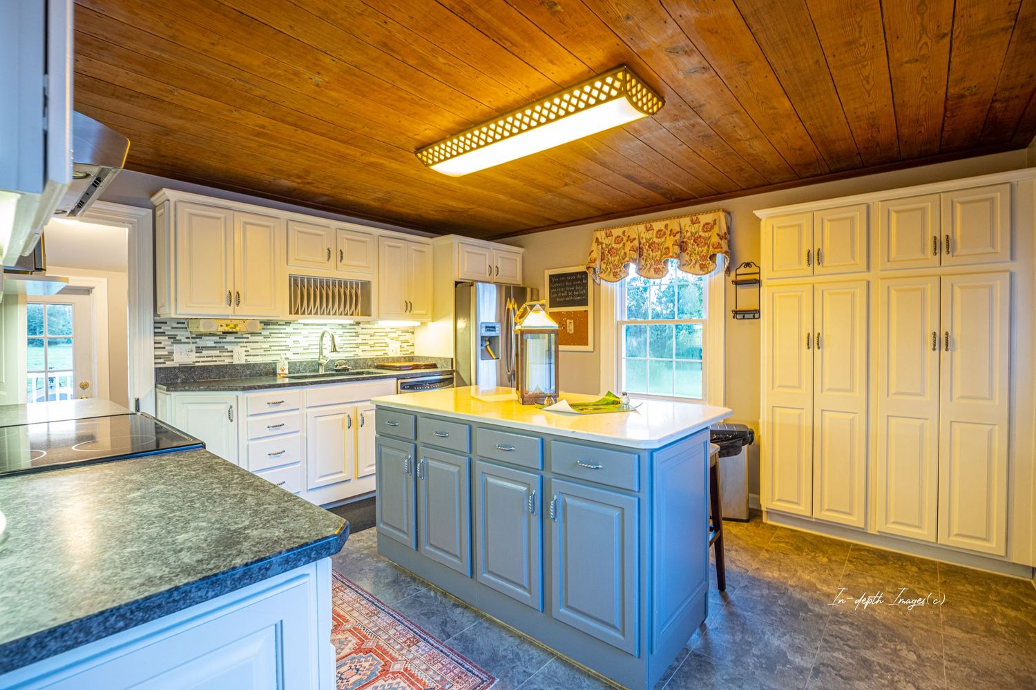 Spacious kitchen with wood ceiling, blue island, white cabinets, and granite countertops in a country home.