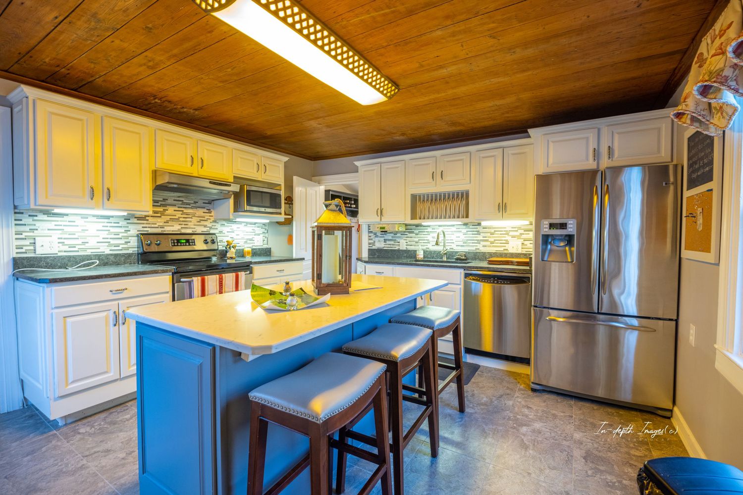 Bright kitchen featuring blue island with seating, stainless steel appliances, white cabinets, and wood ceiling.