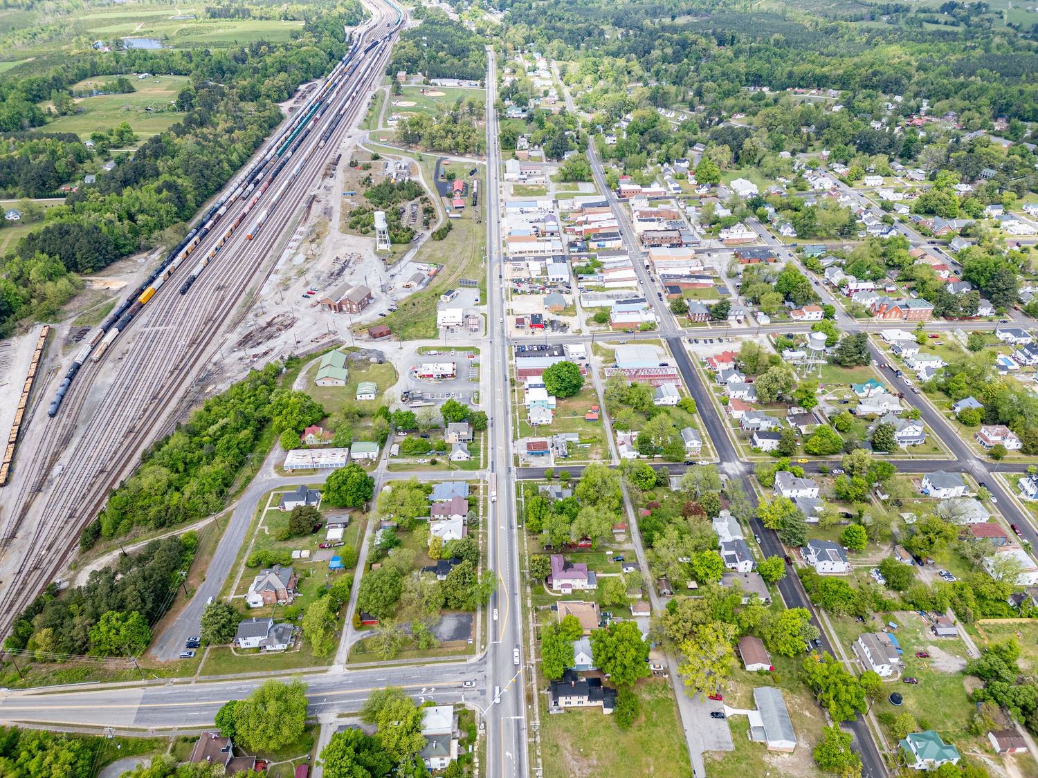 An aerial view of a small town with a railroad yard, residential streets, and lush green trees.