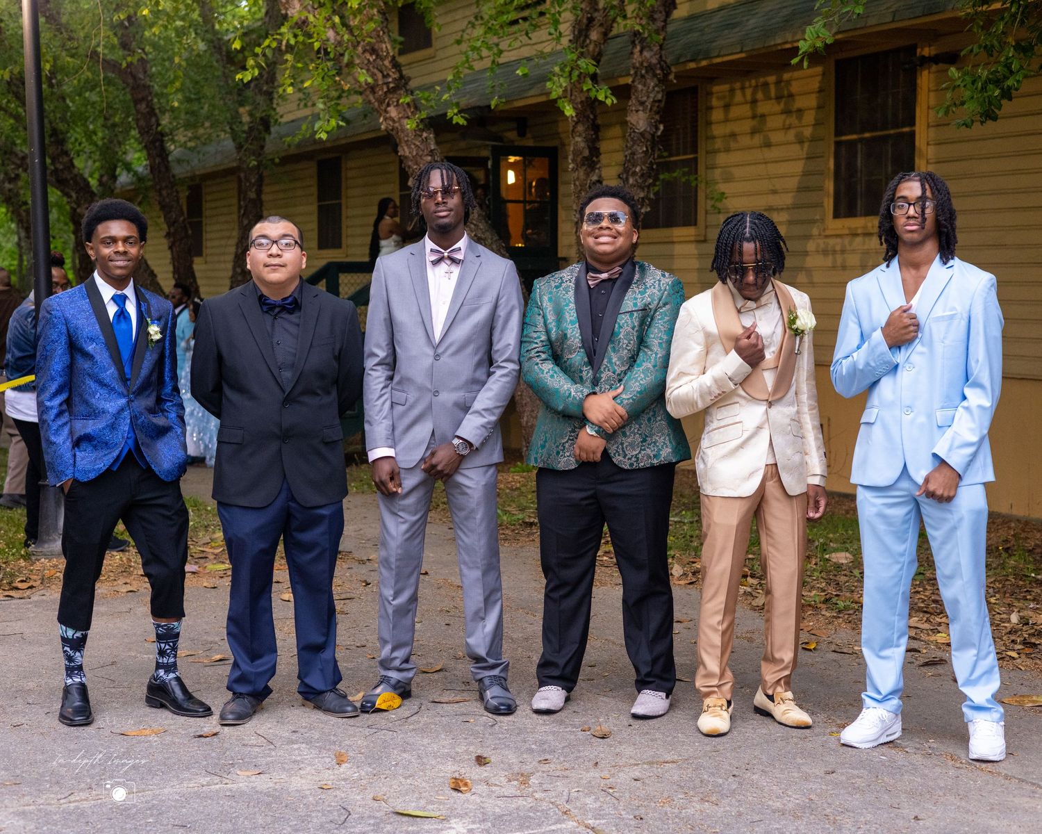 Group of seven young men dressed in formal suits outdoors.
