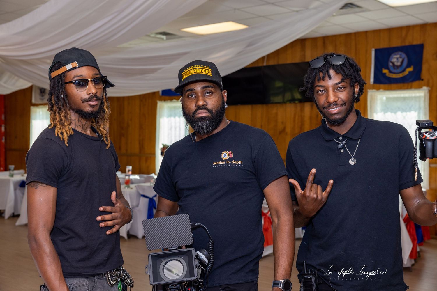 Three men in black shirts posing together at an indoor event with camera equipment.