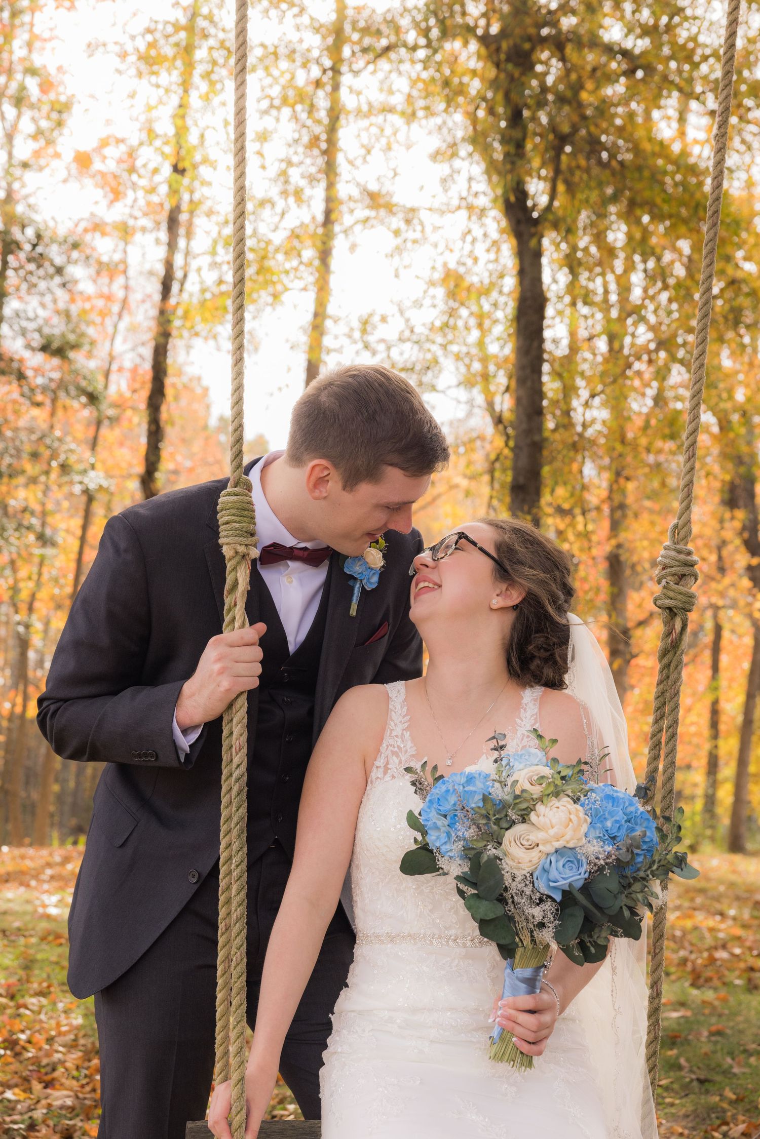 Bride and groom share a tender moment on a rope swing surrounded by autumn foliage.