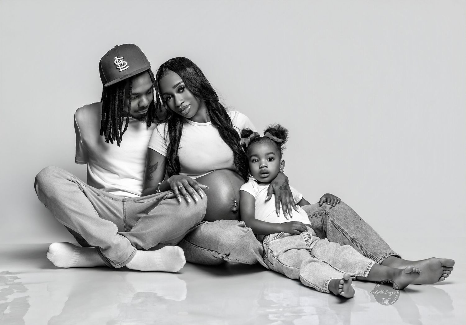 Black and white family maternity photo of couple and toddler sitting together on studio floor.
