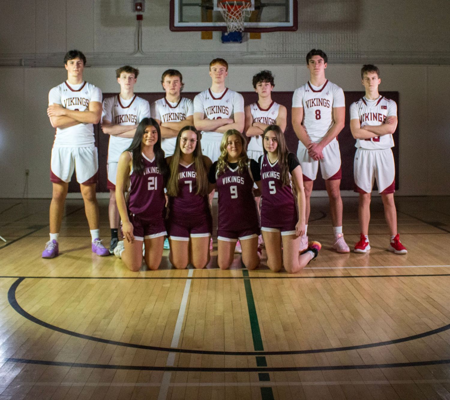 Vikings basketball team poses in gym, boys standing in back row, girls kneeling in front, wearing maroon and white uniforms.