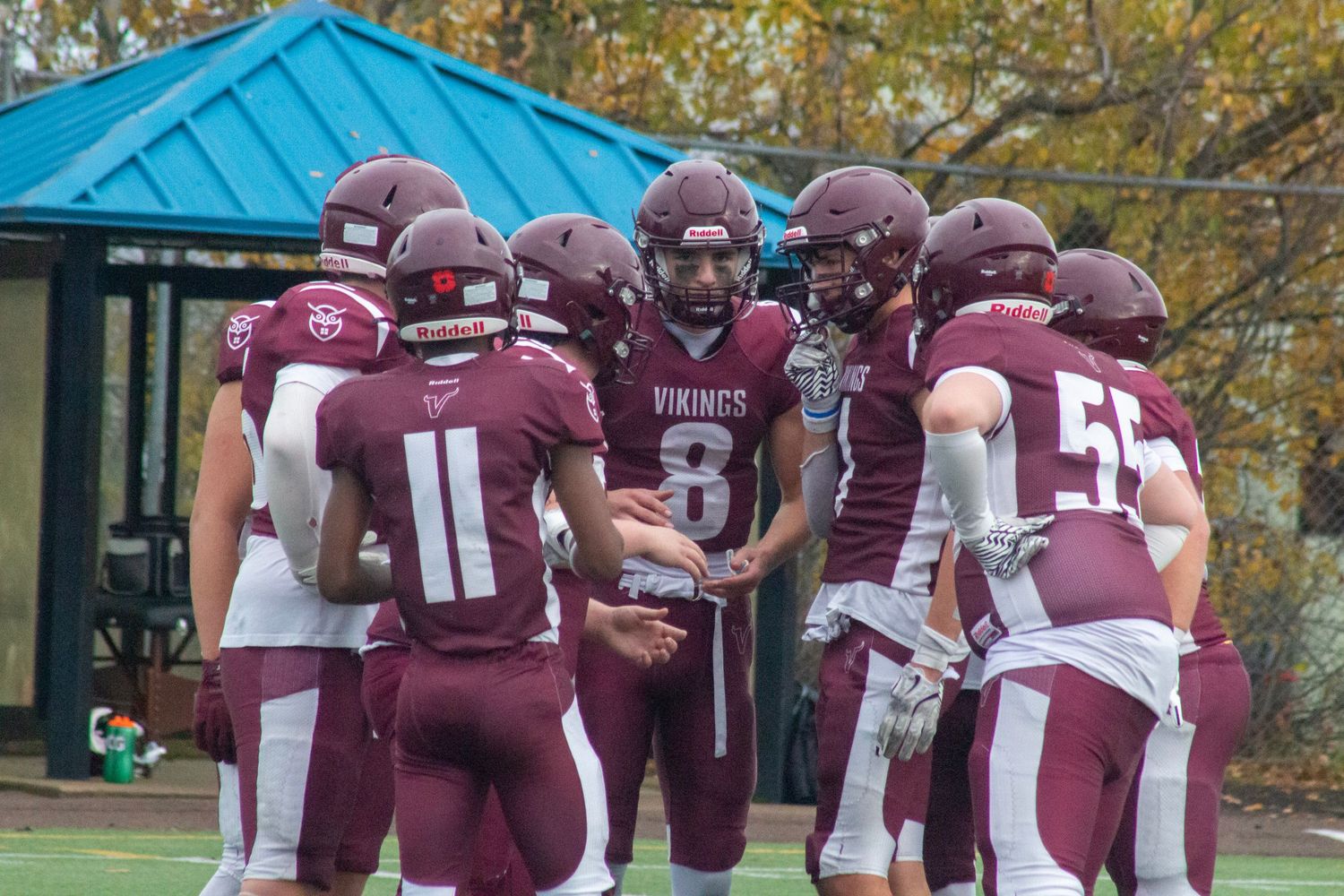 Vikings football team huddles in maroon uniforms, with player #8 leading the huddle on a fall game day.