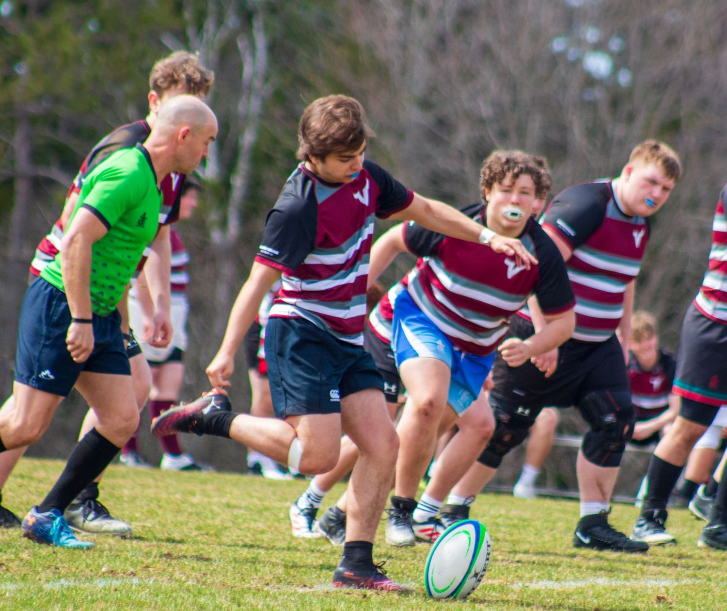 Young rugby players compete in an outdoor match, with one player kicking the ball during an intense youth rugby game.