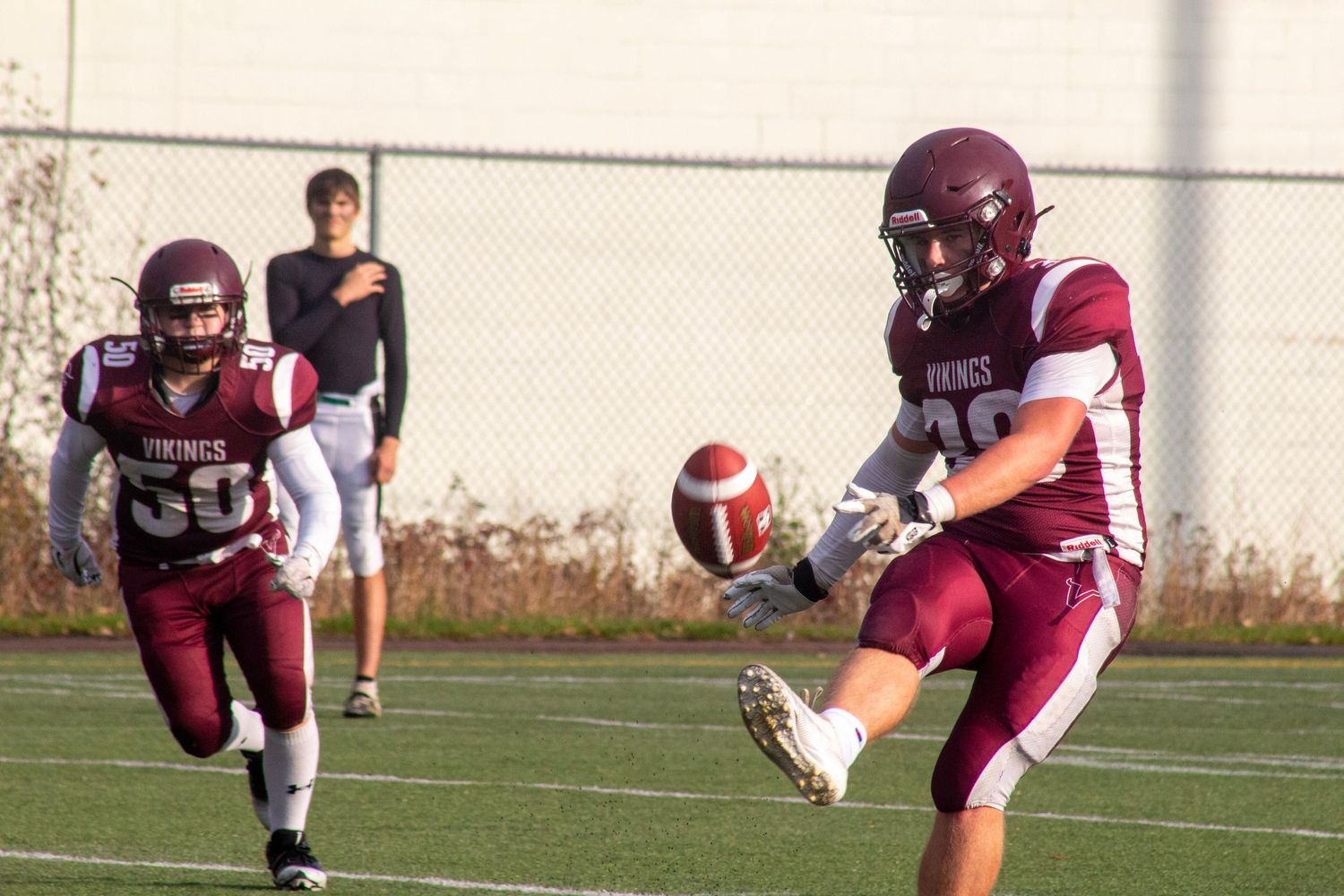 Two youth football players in maroon uniforms during a punt play on a sunny day.