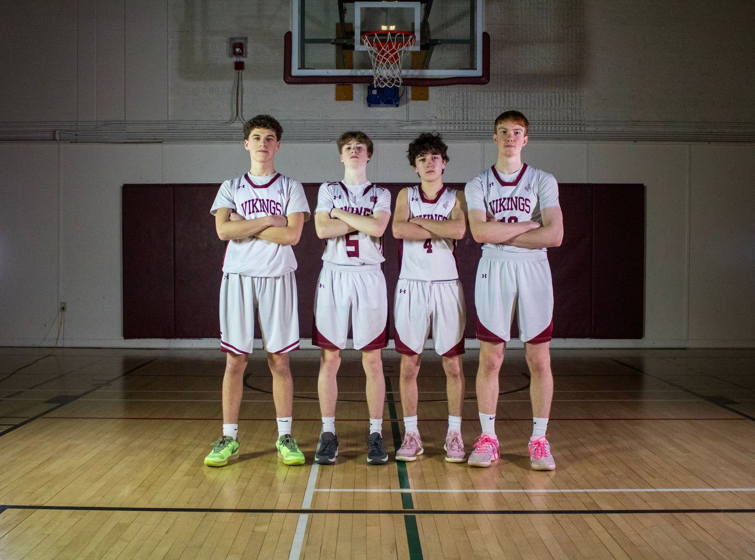Four male high school basketball players in white uniforms pose together on an indoor court.