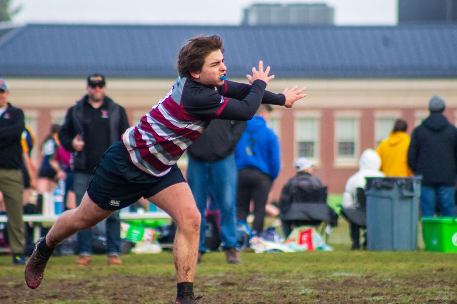 Player throwing a rugby on a muddy field during an rugby tournament outdoors.