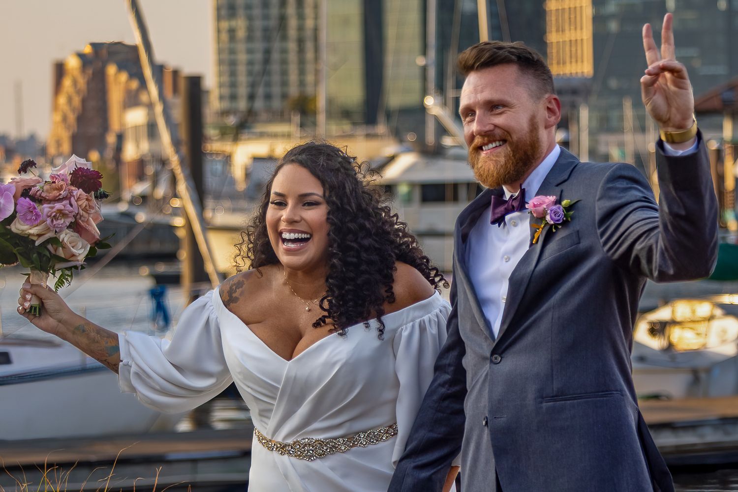 Wedding party celebrates joyfully with arms raised during outdoor celebration at sunset.