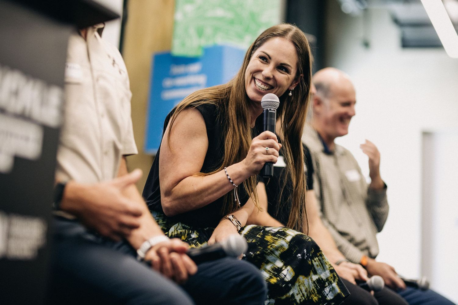 A woman speaking on a panel smiles whilst holding a microphone.