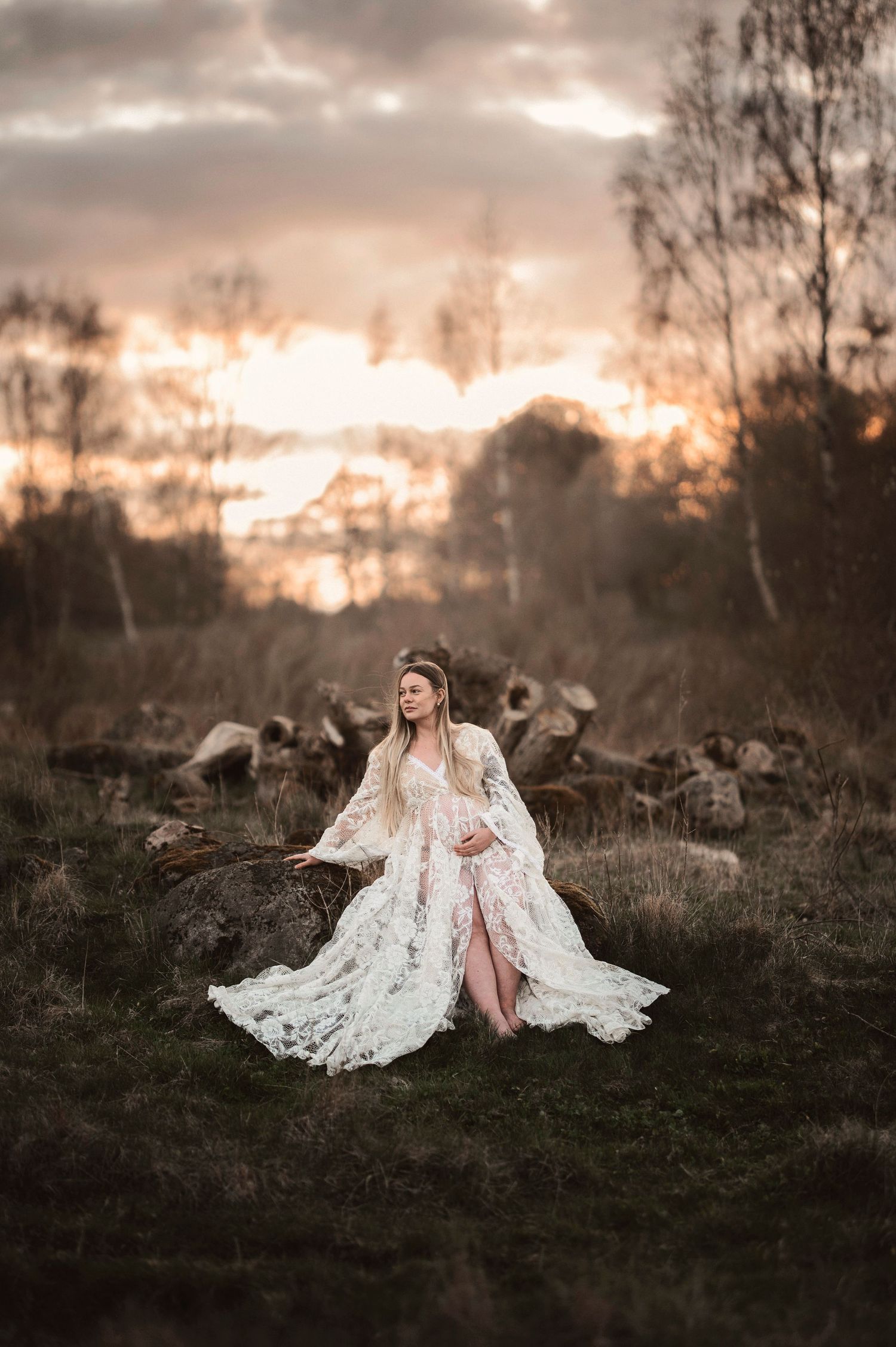 A dreamy sunset scene features an ethereal white lace dress against a dramatic sky and forest backdrop.