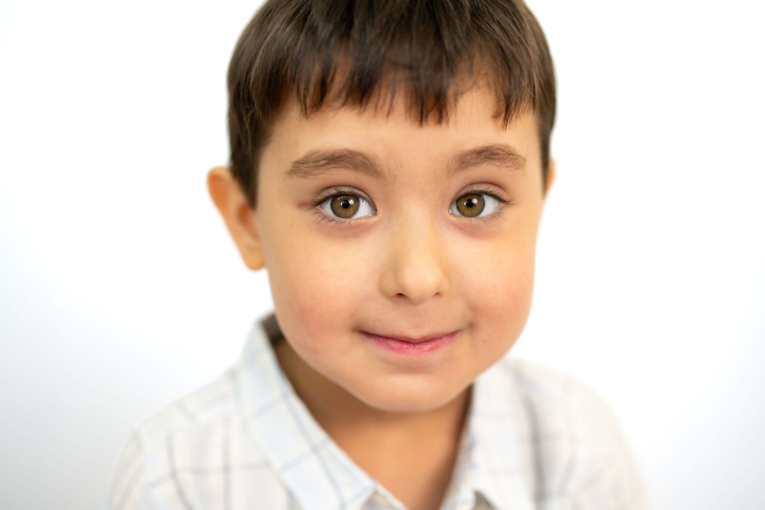 Close-up portrait of a young boy with dark hair in a plaid shirt smiling.