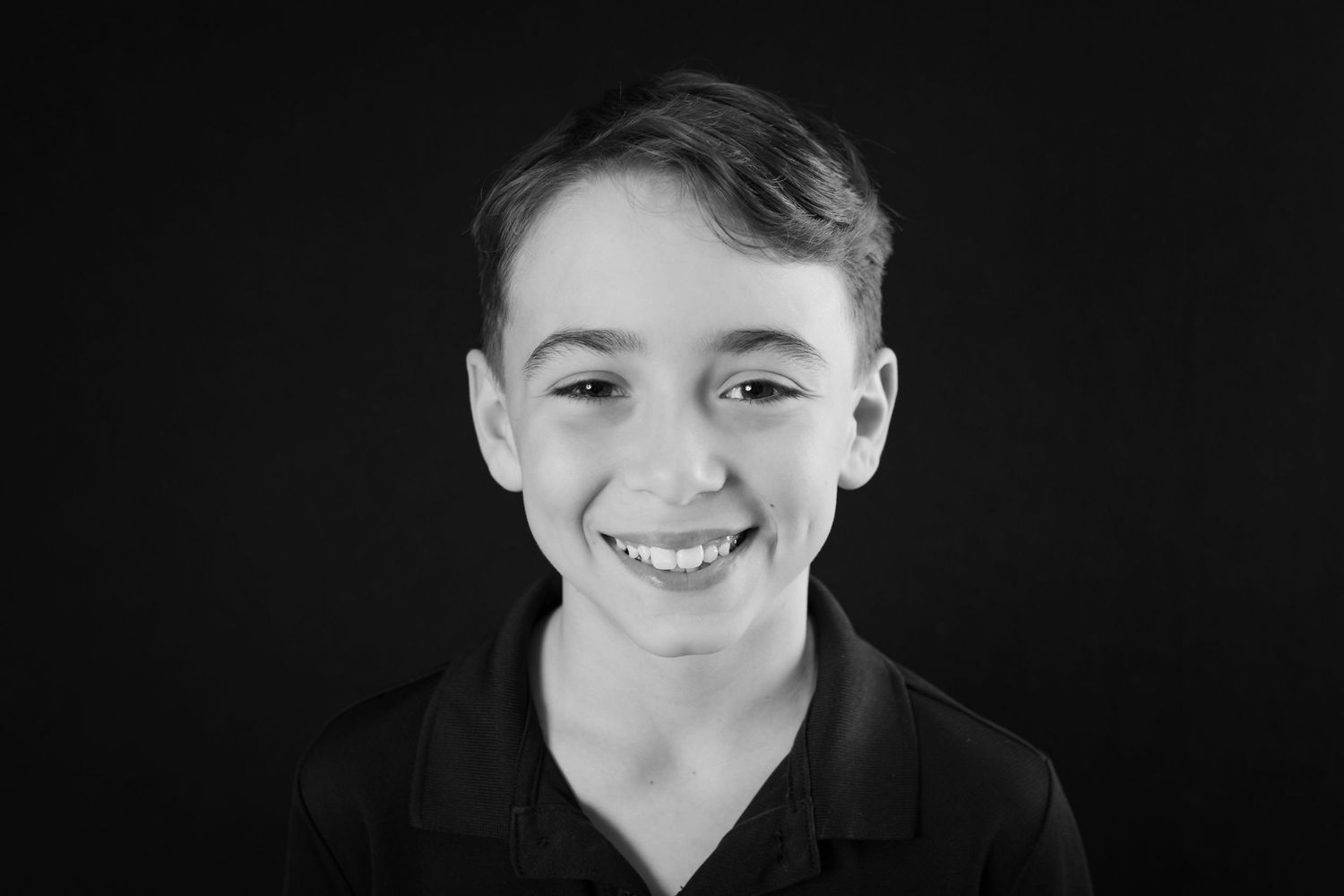 Black and white portrait of a smiling young boy with short hair wearing a dark polo shirt.