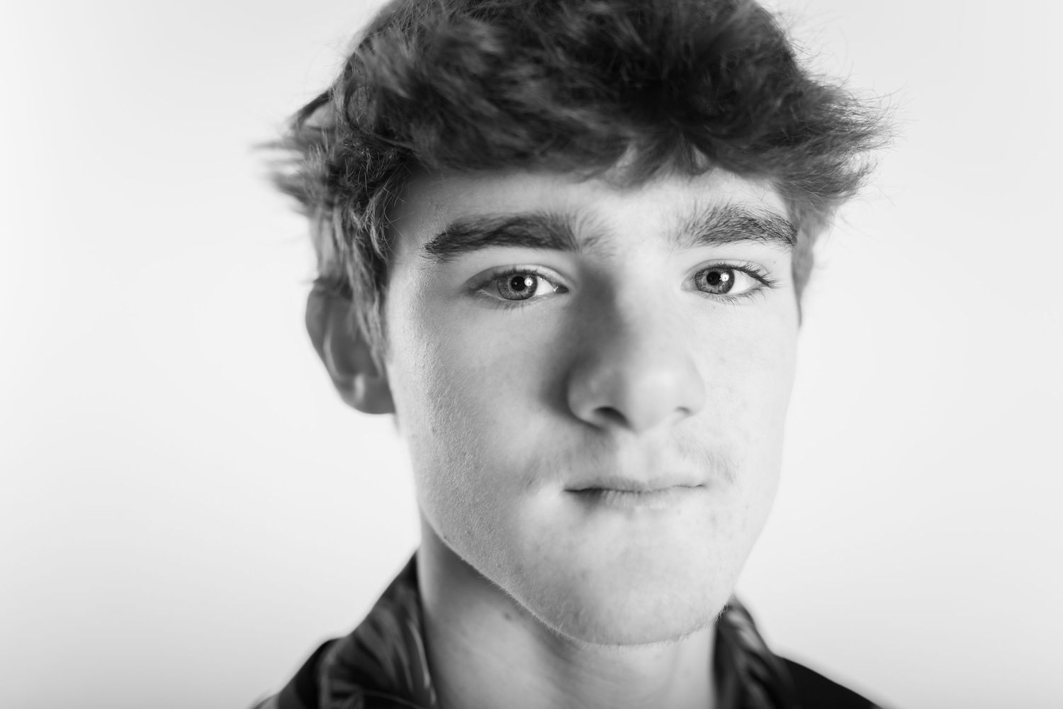 Black and white close-up portrait of a teenage boy with curly hair smiling.