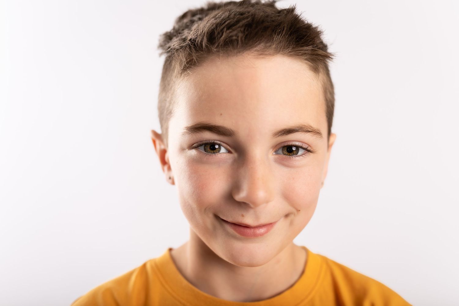 Young boy in a yellow t-shirt smiling confidently against a white background.
