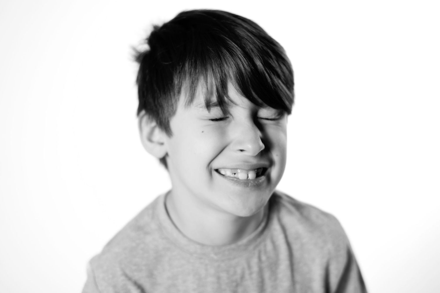 Black and white photo of a boy smiling with eyes closed wearing a gray t-shirt.
