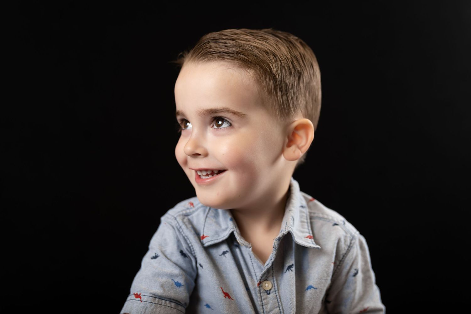 Happy young boy in blue shirt smiling and looking sideways on black background.