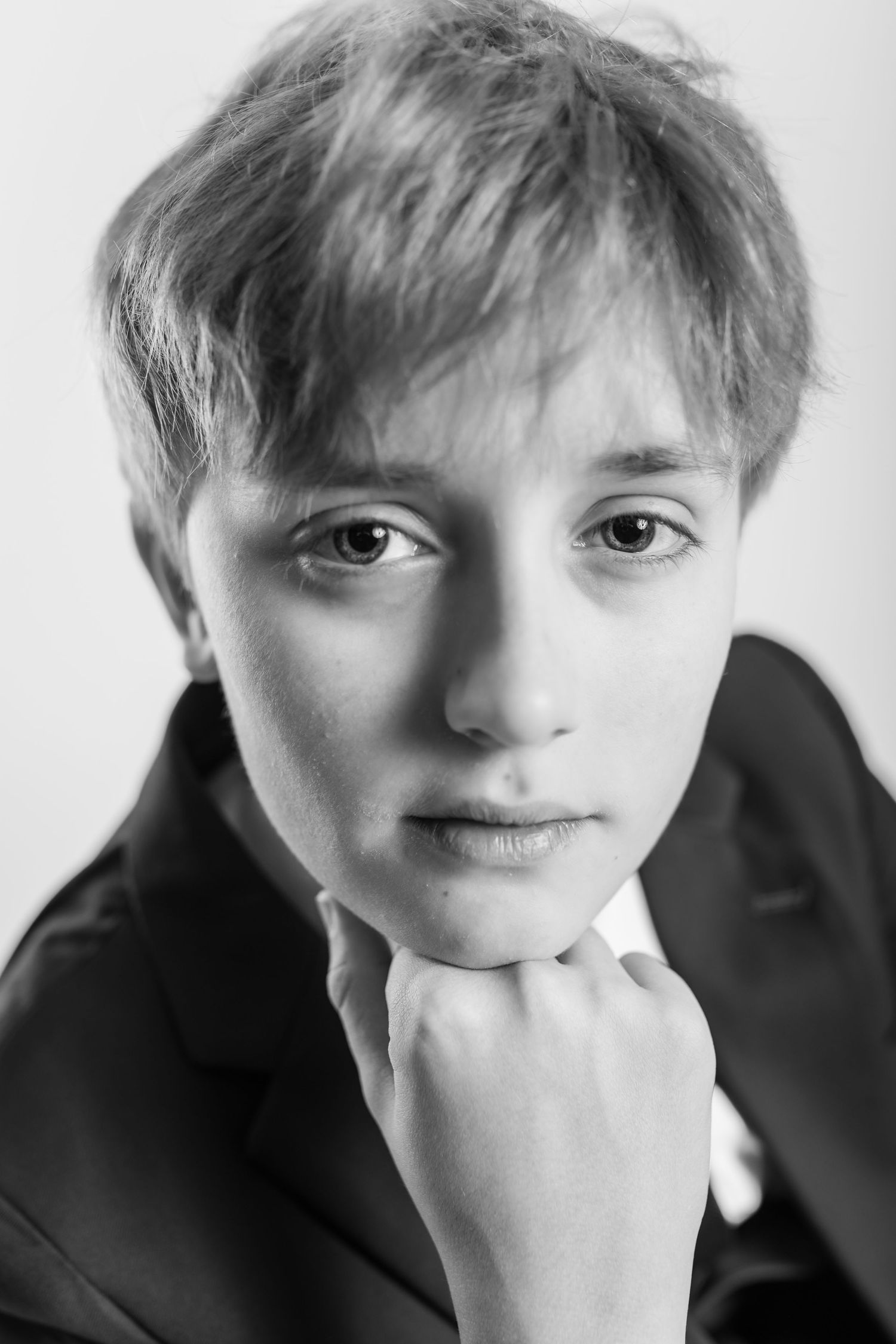 Black and white portrait of a young boy in a suit resting his chin on his hand.