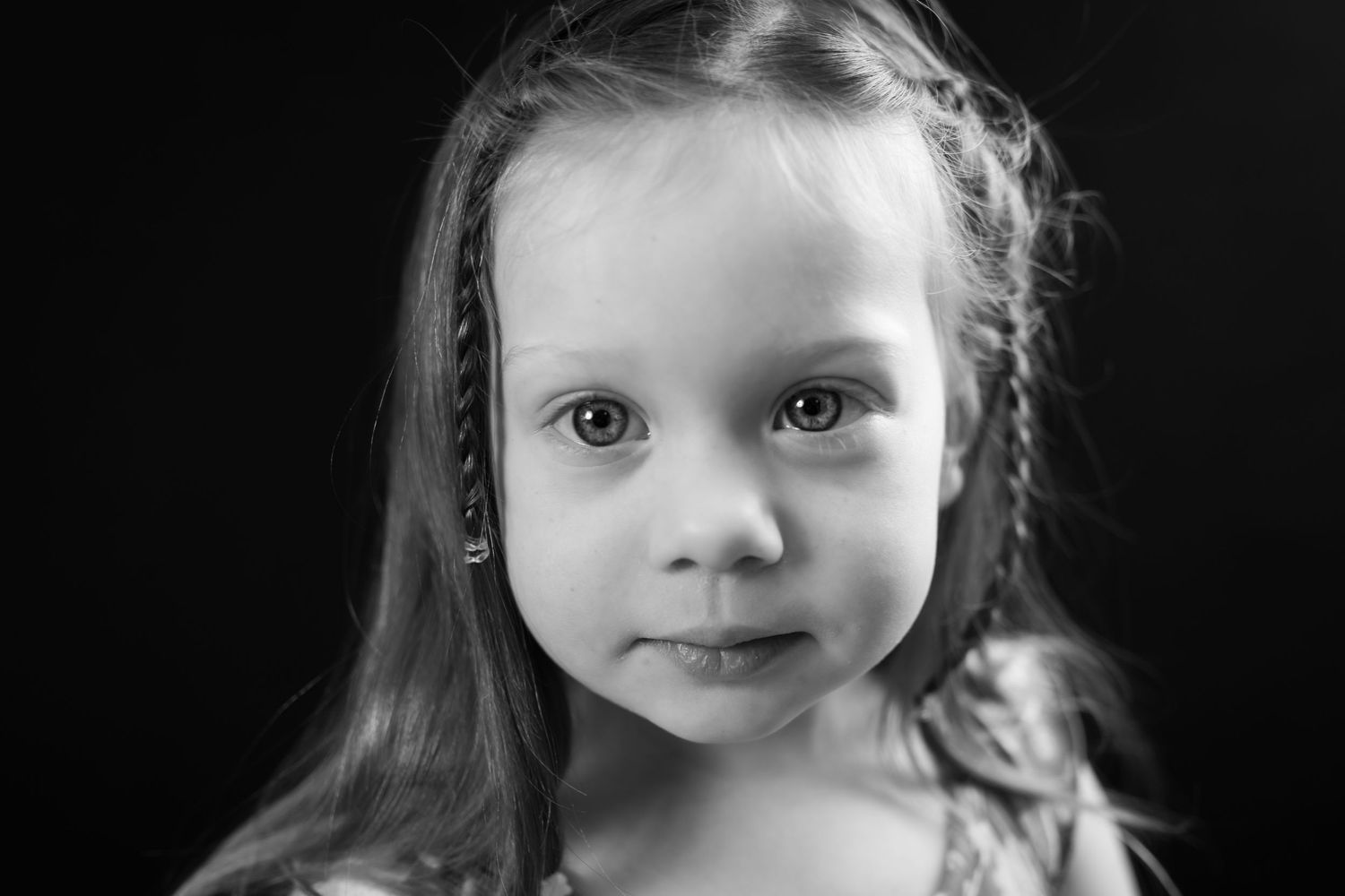 Black and white portrait of a young girl with braided hair gazing at the camera.