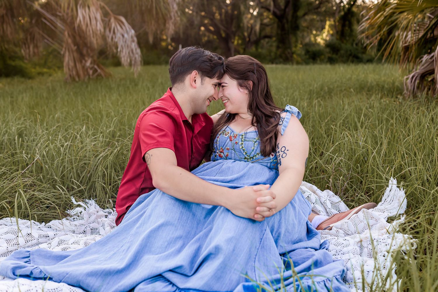 A couple sits in a green field, leaning close together, the woman wearing a blue gown.