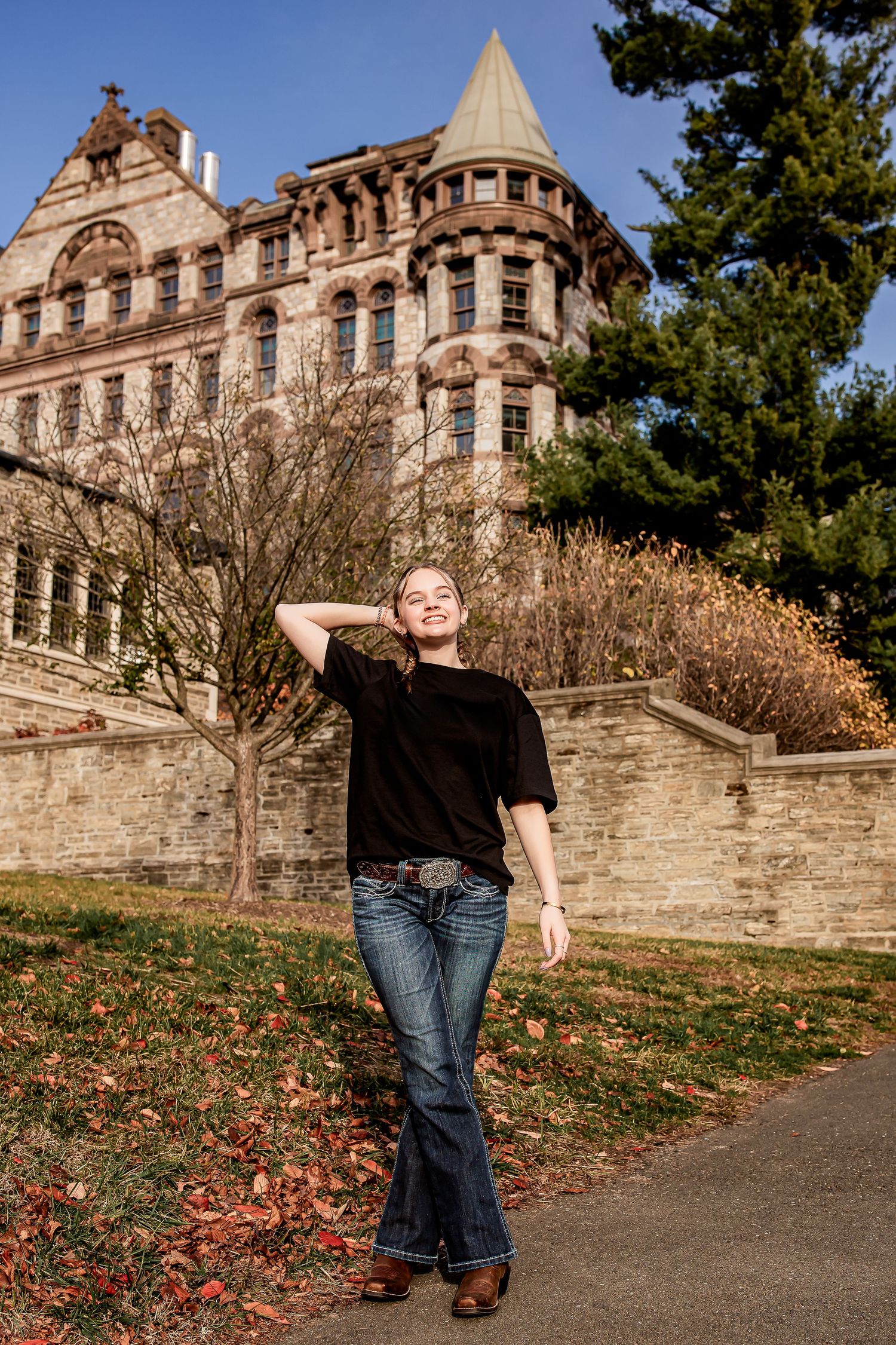 Young woman in black top and flared jeans posing before a historic stone building.