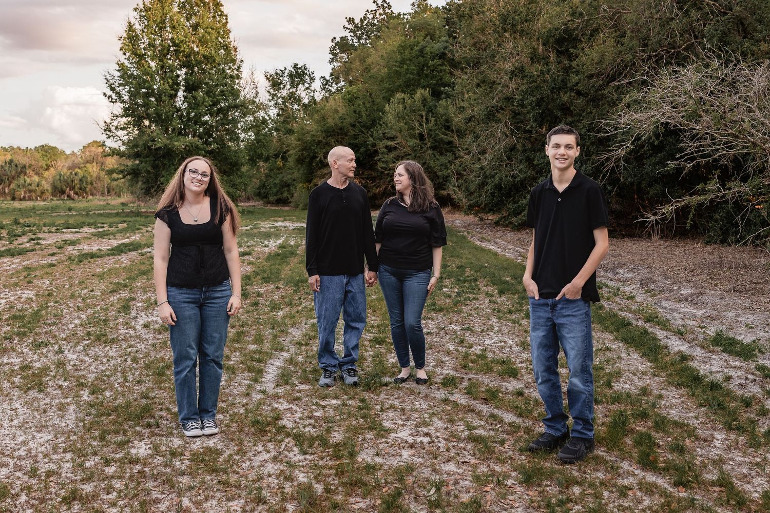Family of four in matching black tops and jeans posing in an open field.