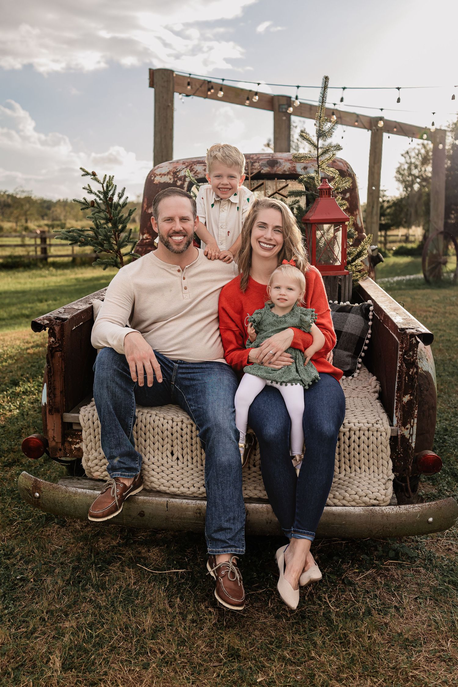 Happy family of four sitting on a vintage truck bed decorated for Christmas on a farm.