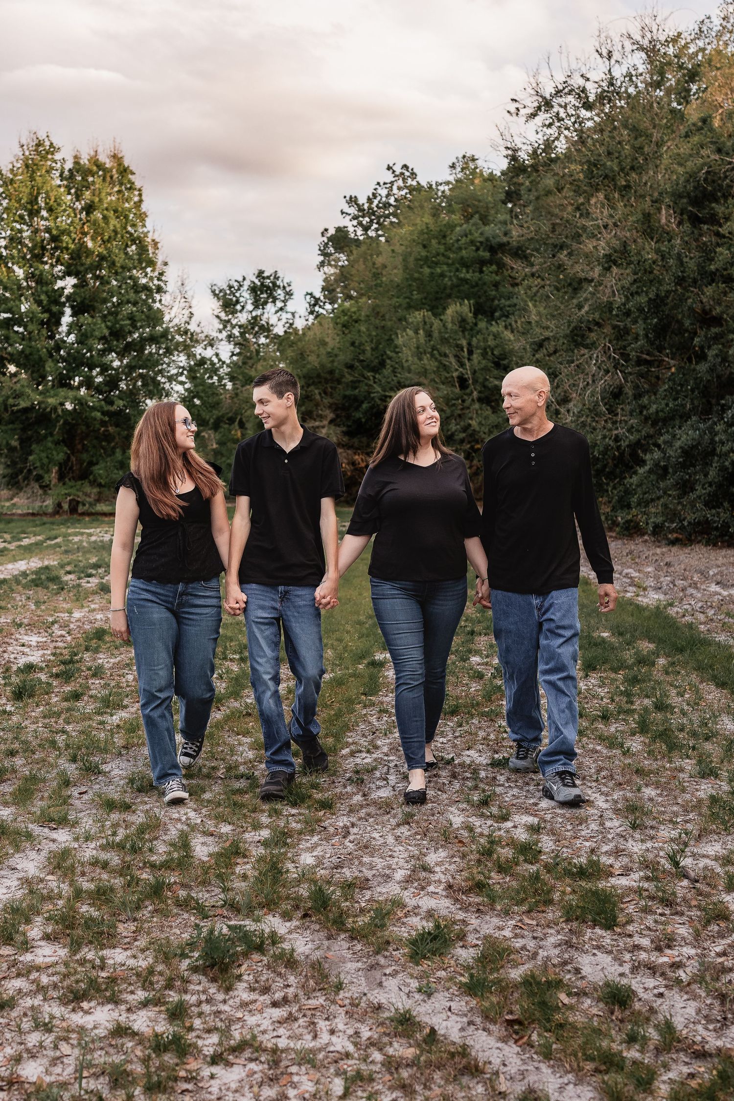 Family of four holding hands and walking together in a green outdoor setting.