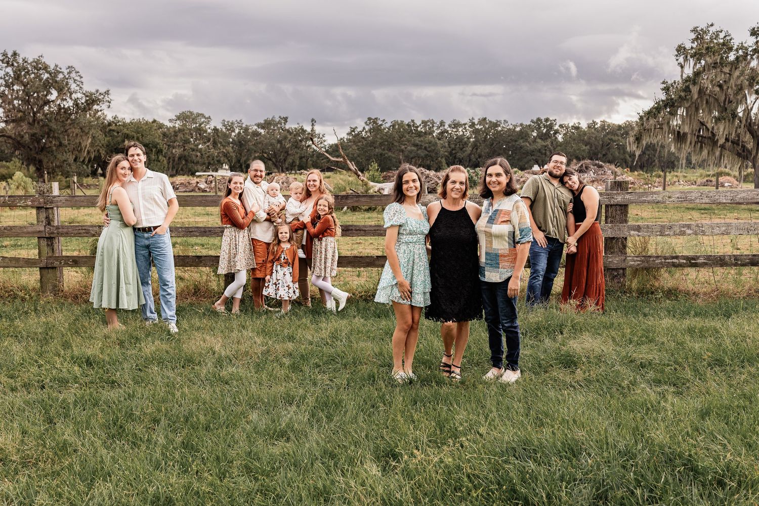 Large family group posing together in a green field with wooden fence at golden hour.