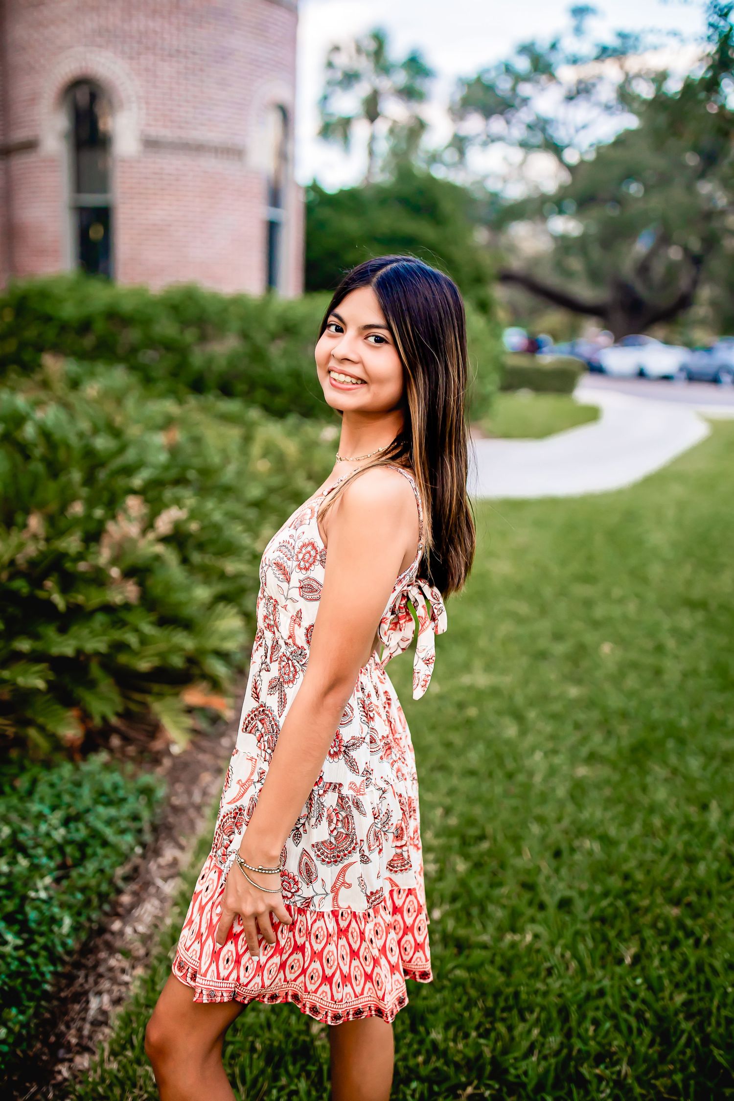 Young woman in floral sundress posing outdoors near brick building.