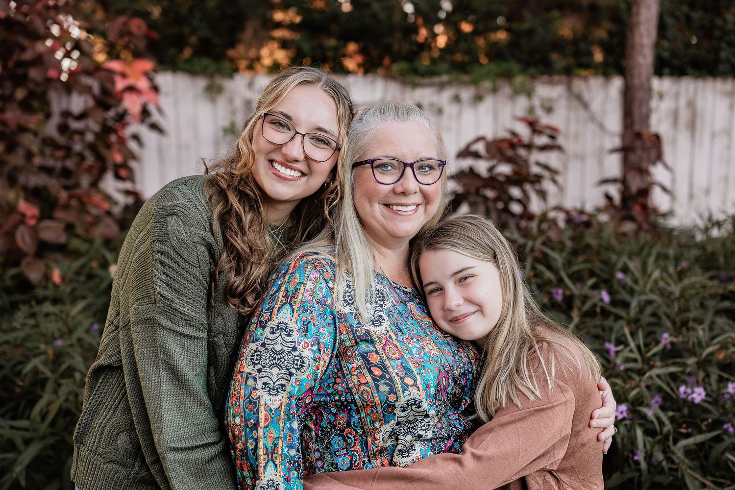 Three generations of women smile and hug together in a garden setting.