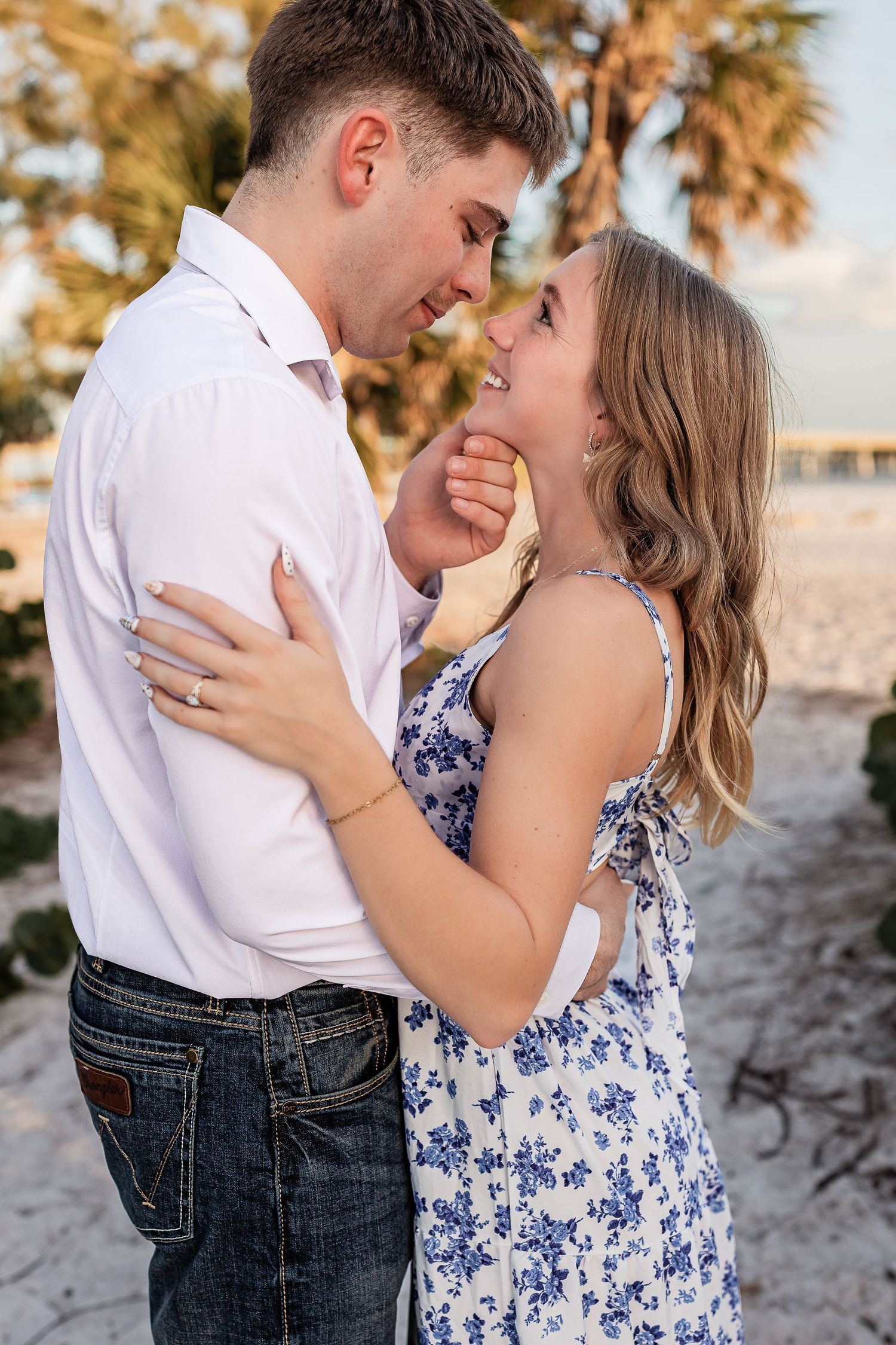 Young couple sharing a romantic moment on a sunny beach with palm trees behind them.