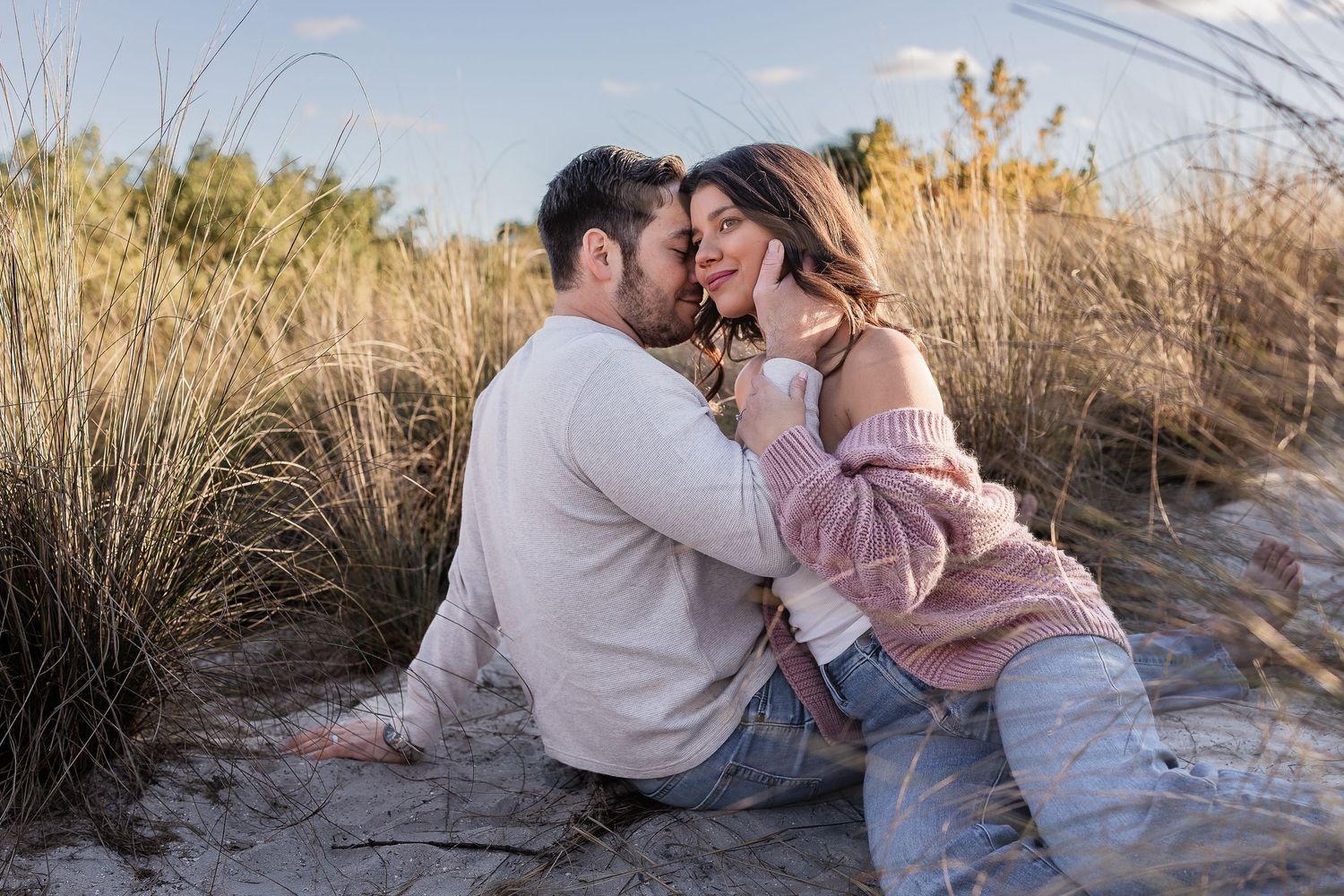 Couple sharing a kiss while sitting in sandy beach dunes with golden sea oats around them.
