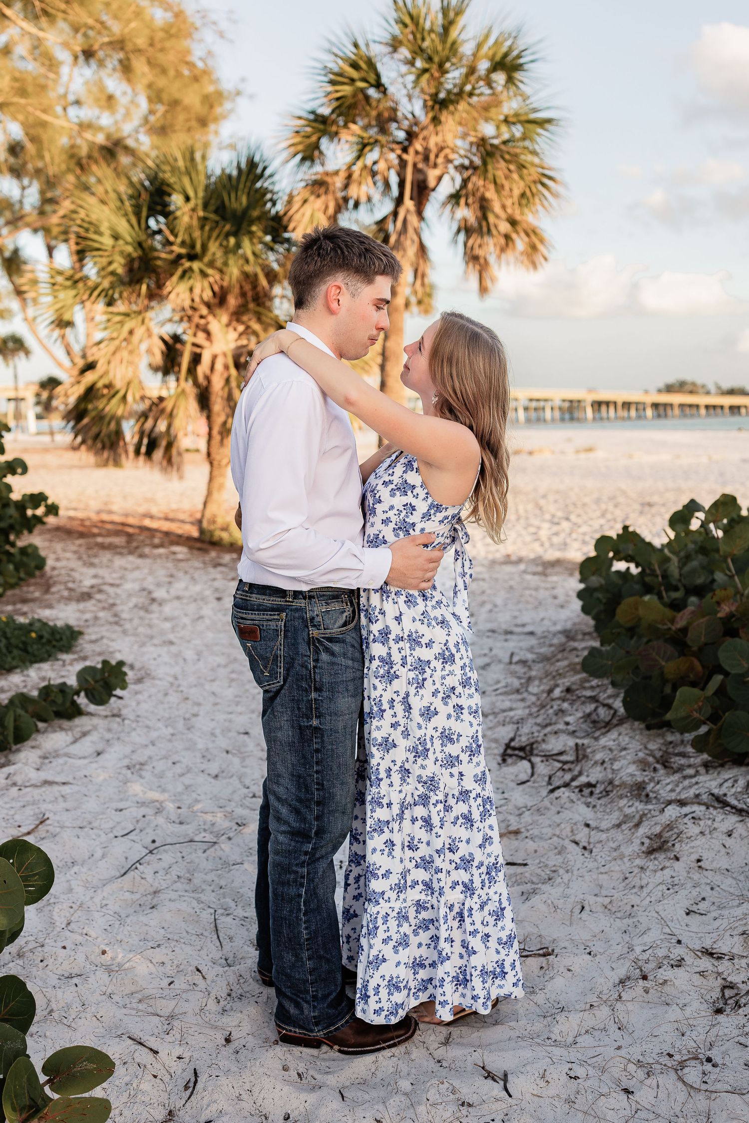 Couple embracing and almost kissing on a sandy beach with palm trees at golden hour.