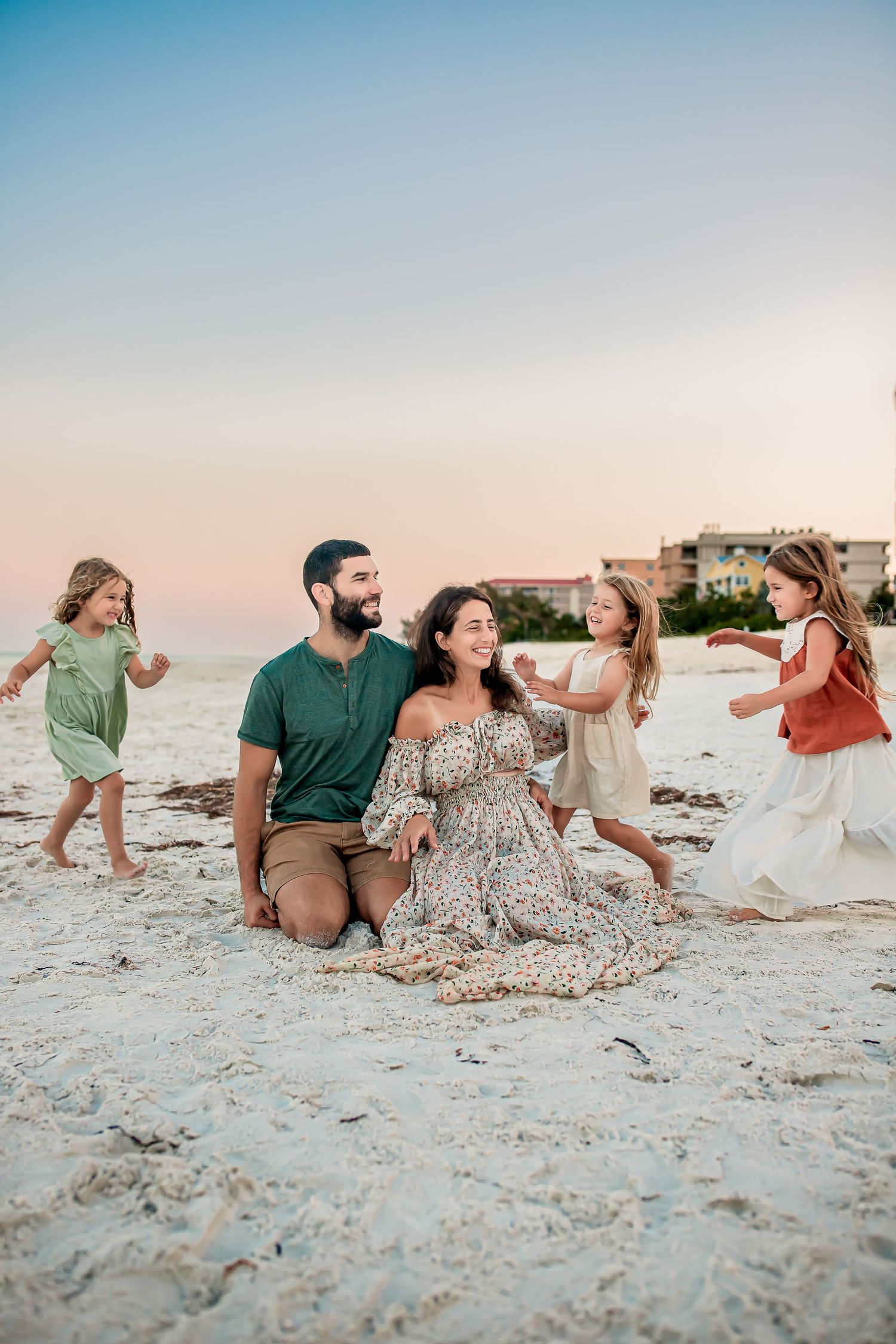 Happy family with three young girls playing on a sandy beach at sunset.