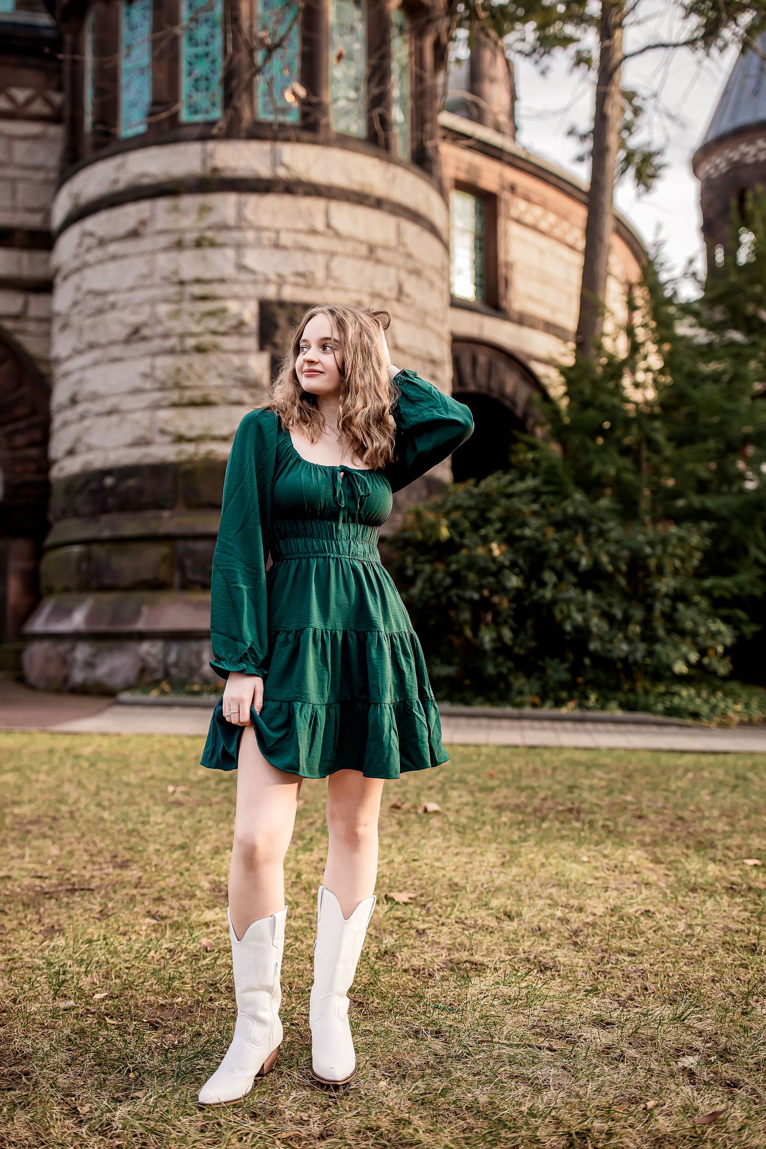 Young woman in green mini dress and white cowboy boots posing in front of a stone castle building.