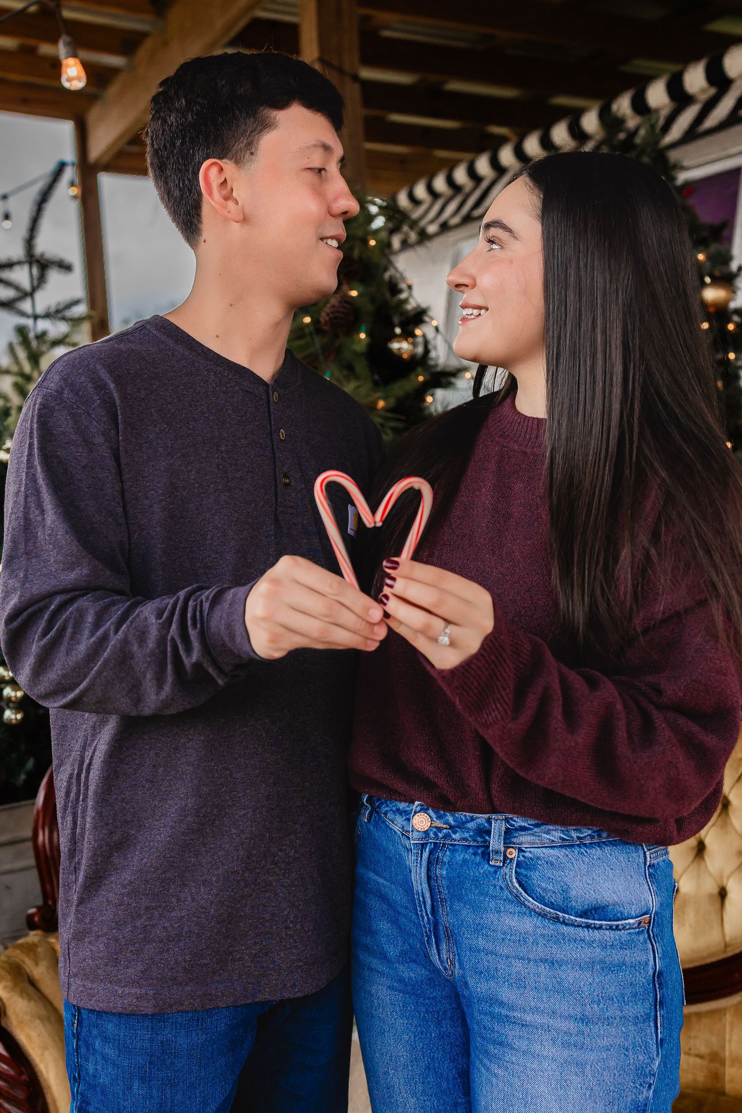 Young couple sharing a romantic moment holding candy canes in a heart shape near a Christmas tree.