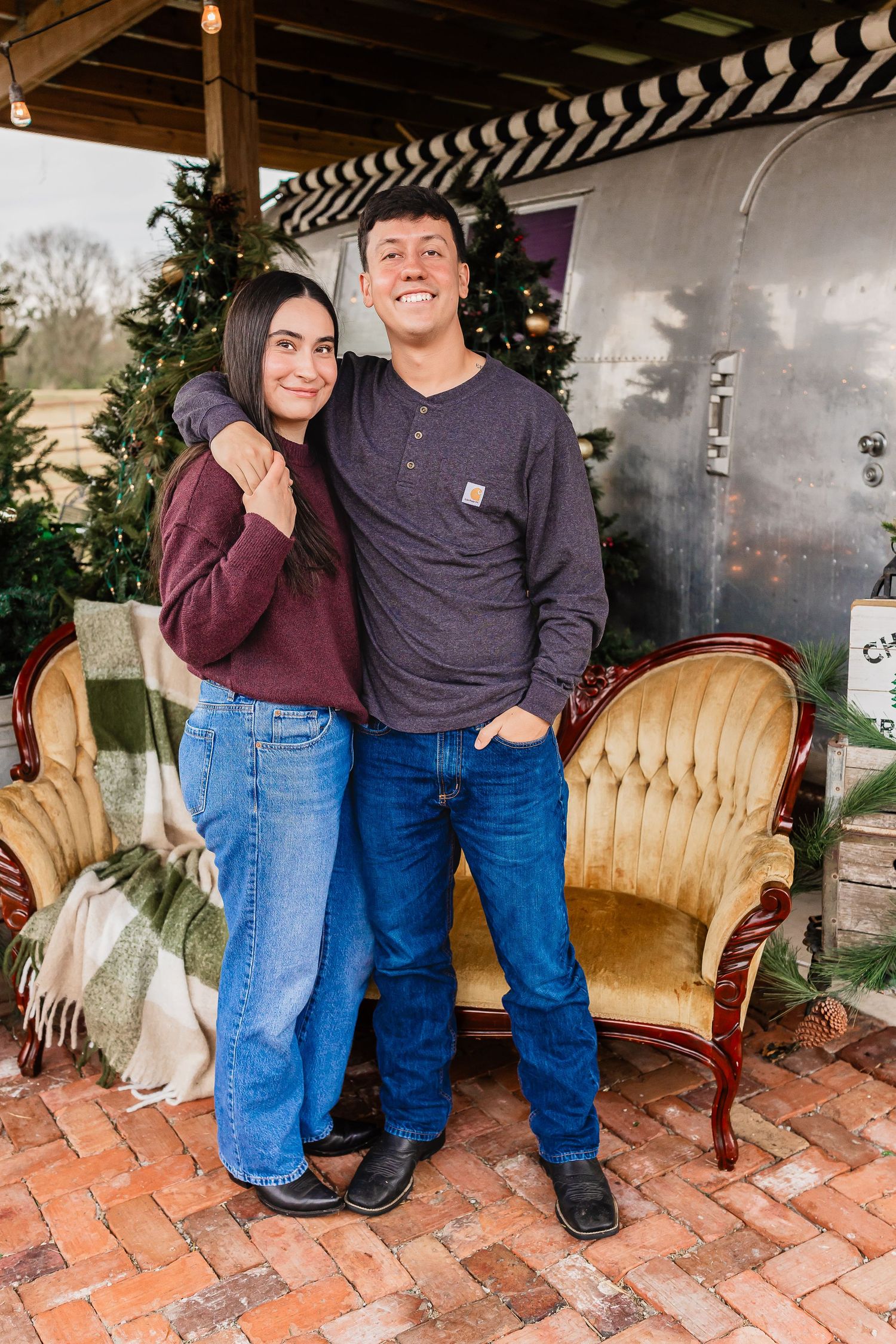 Young couple posing together in front of a festive Christmas backdrop with vintage furniture.