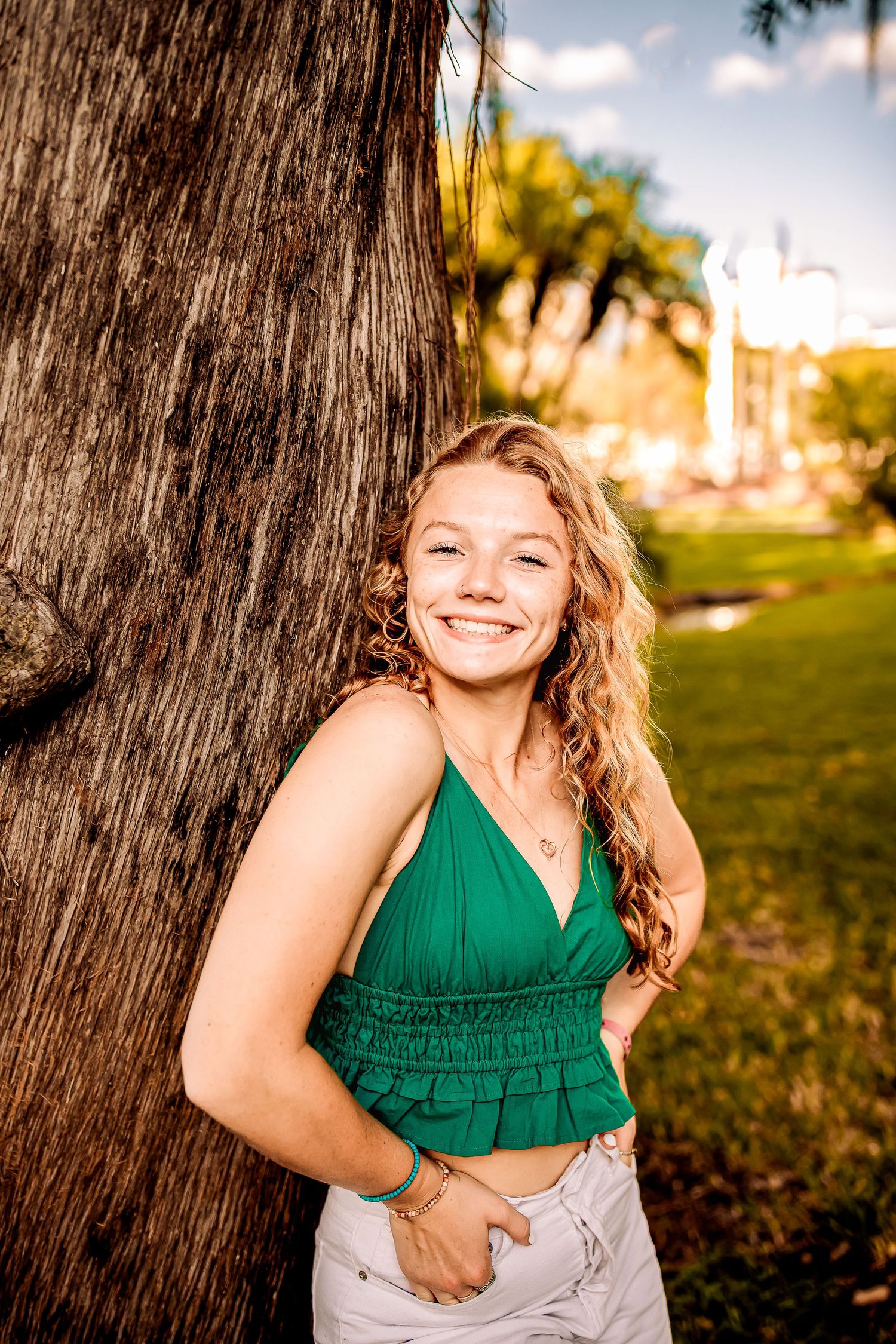 Young girl with curly blonde hair leaning against a palm tree at golden hour.