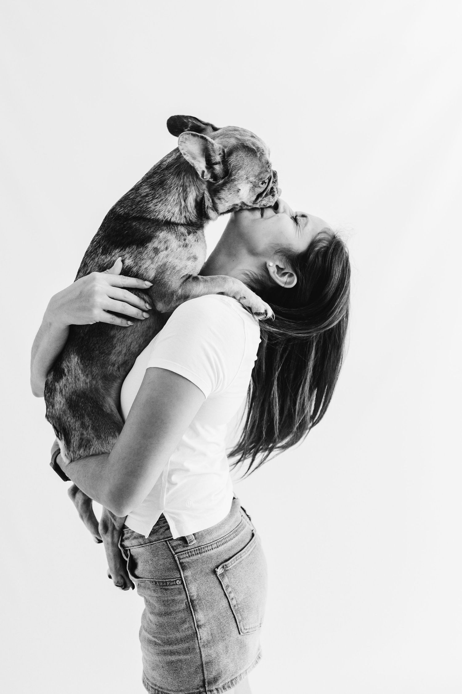 Black and white photo of woman in white tee kissing small dog held above her head.