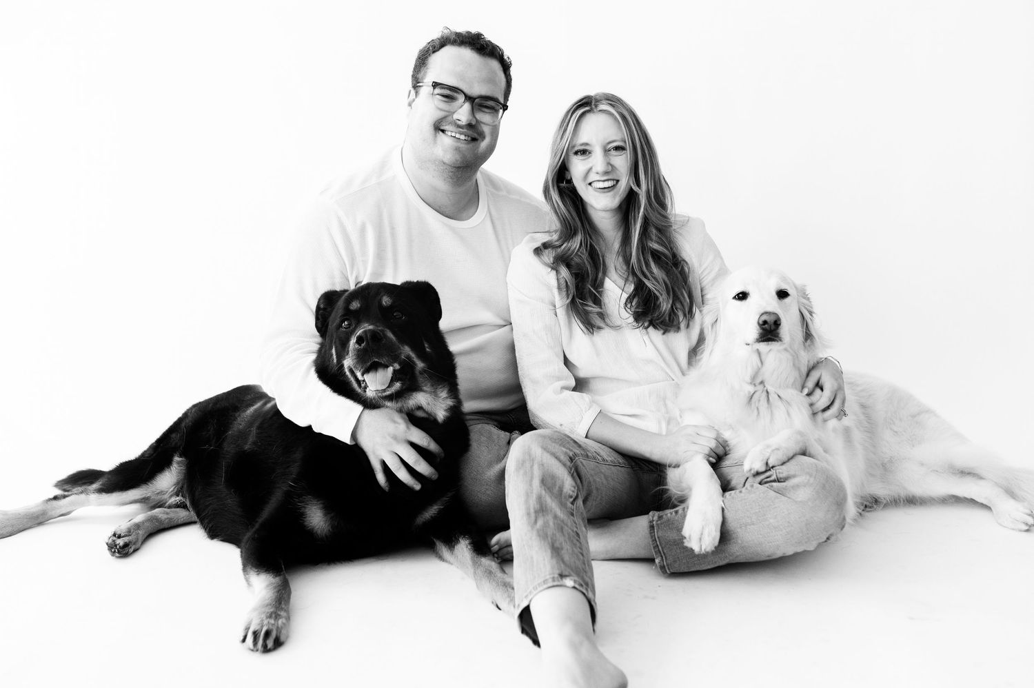 Black and white portrait of couple sitting with a Rottweiler and Golden Retriever.