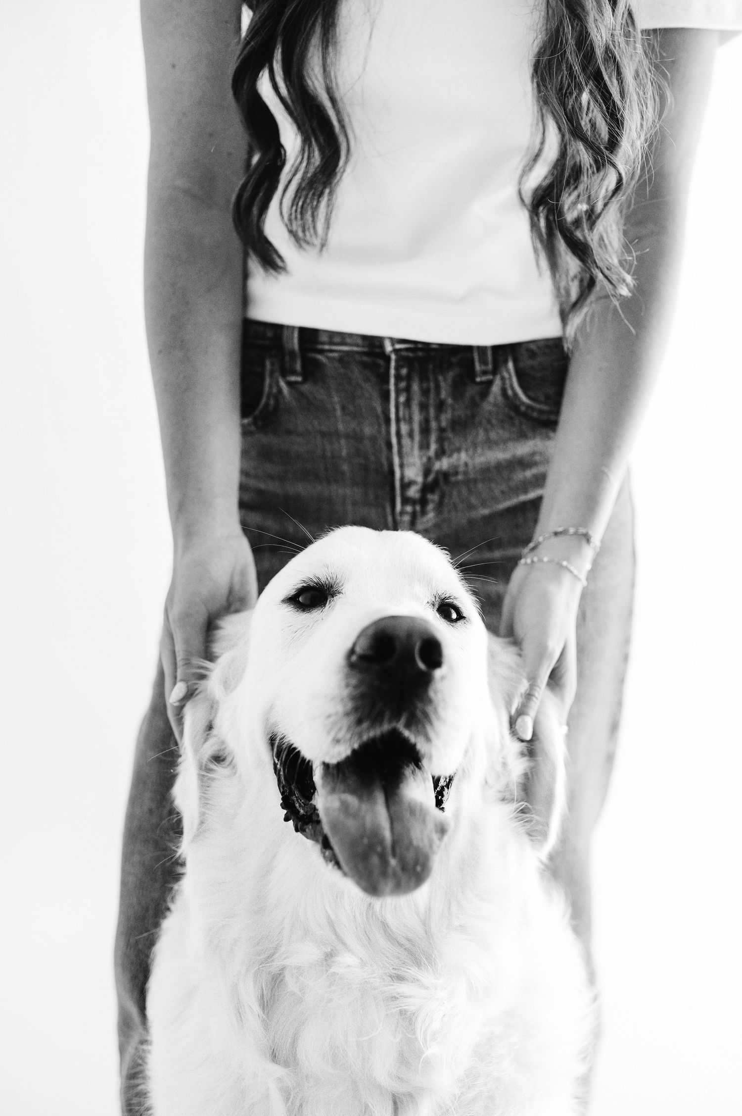 Black and white photo of woman in jeans petting a happy Golden Retriever dog.