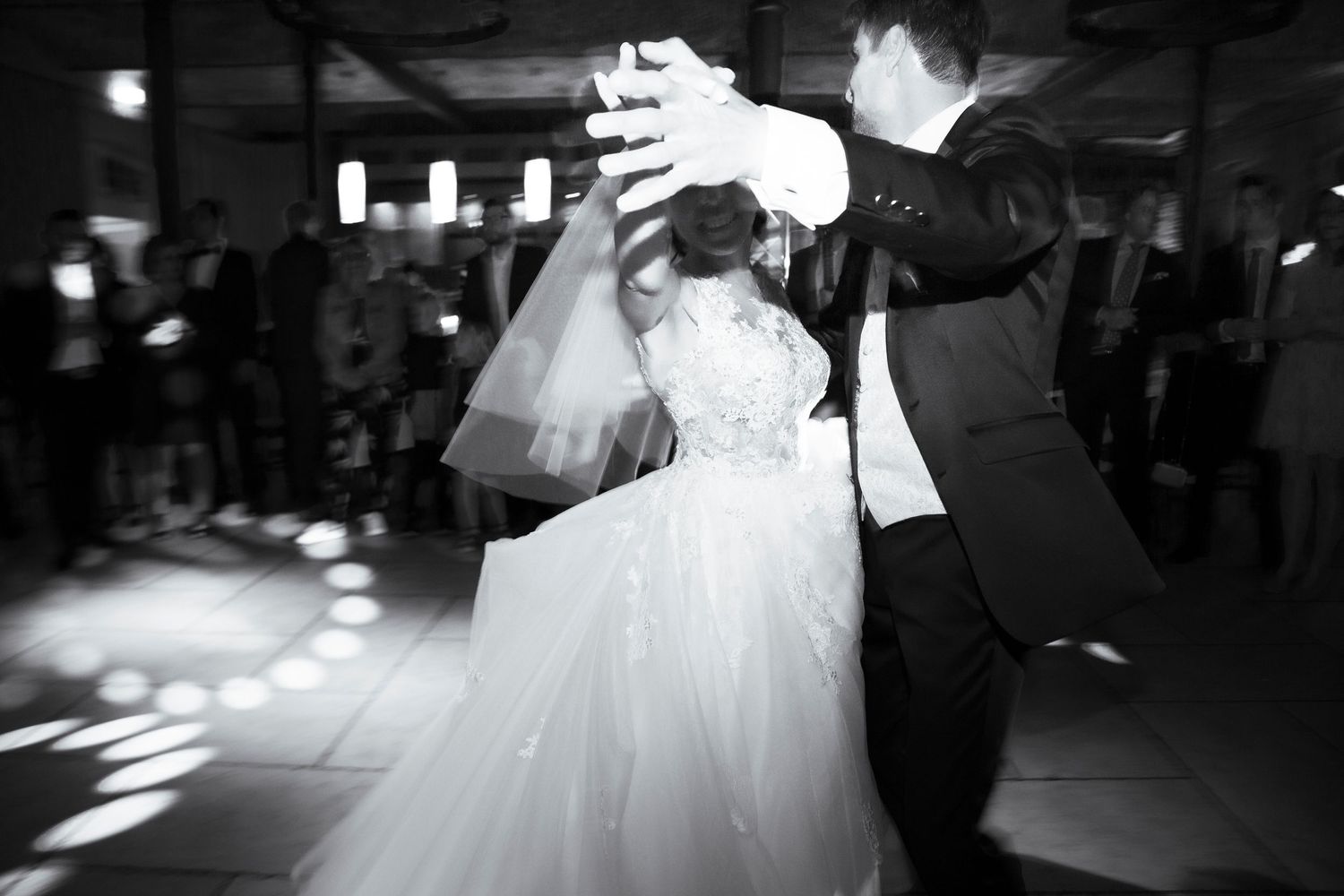 Bride and groom sharing romantic first dance on illuminated dance floor, black and white wedding photo.