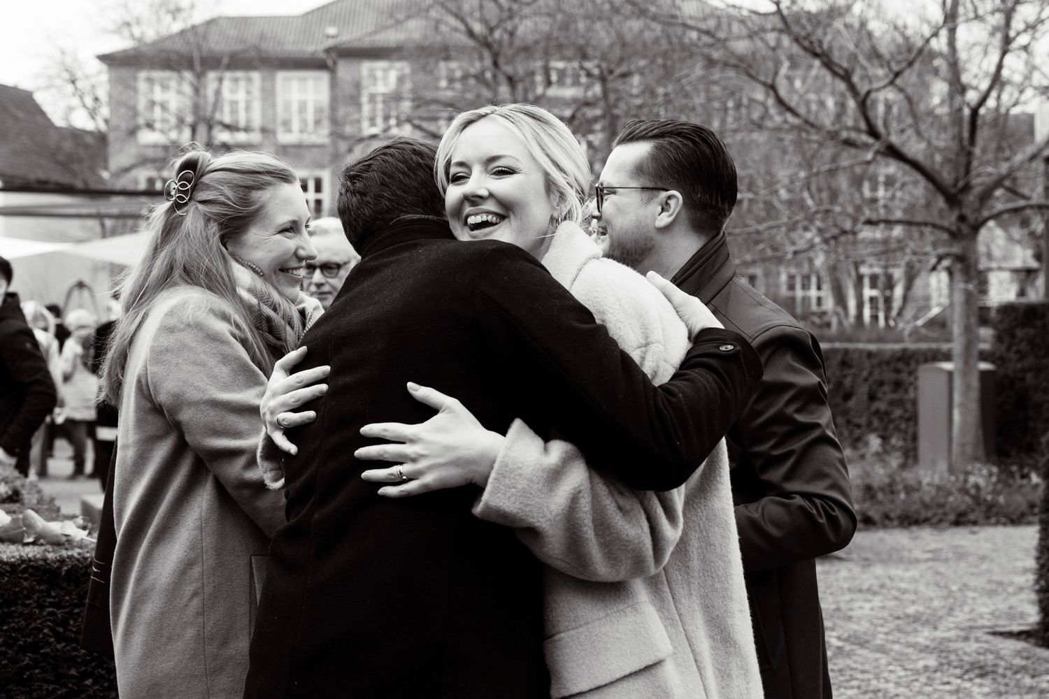 Black and white photo of wedding guests sharing warm embraces and hugs outdoors at a winter wedding.