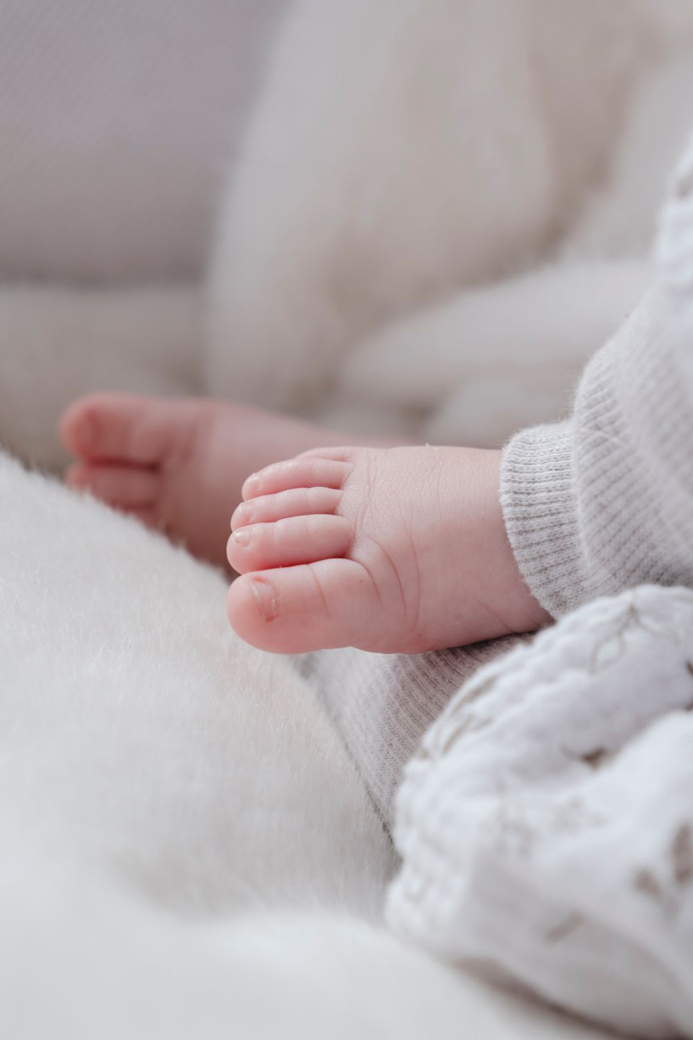 Close-up of tiny newborn baby foot peeking out from soft white knit blanket.