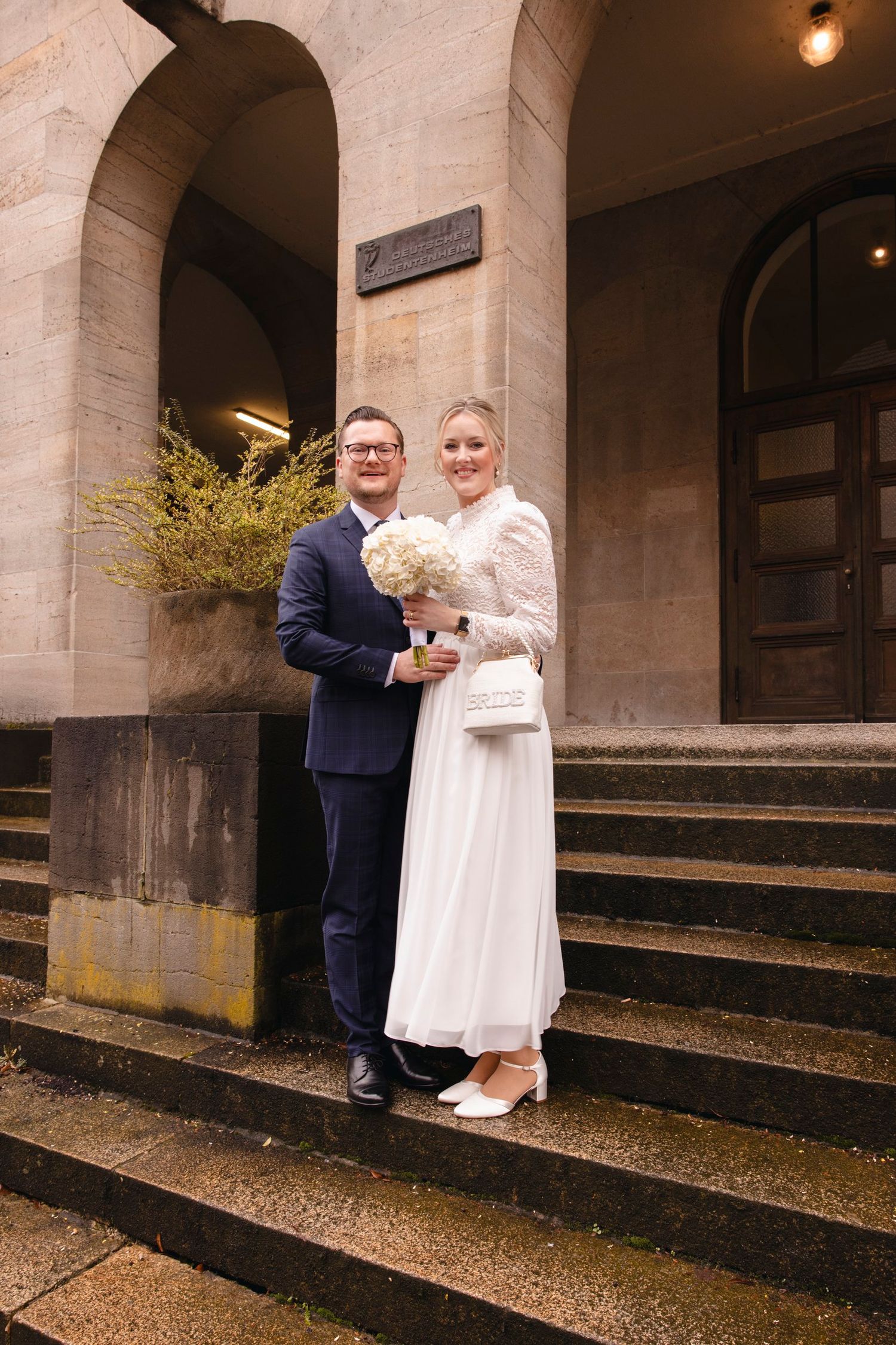 Smiling newlyweds pose on stone steps outside historic building after civil ceremony.