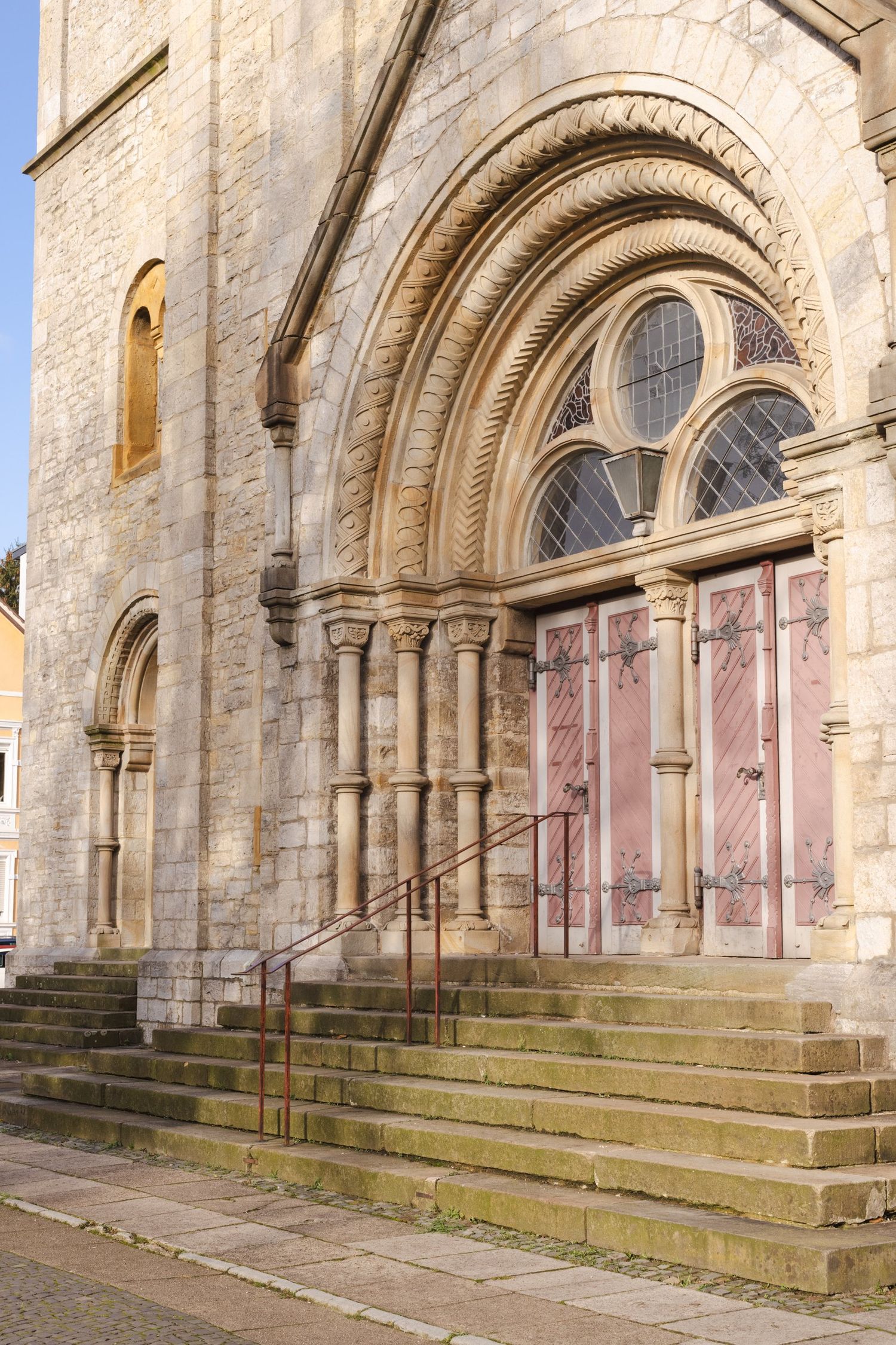 Historic stone church entrance with ornate arched doorway, rose window, and stone steps.